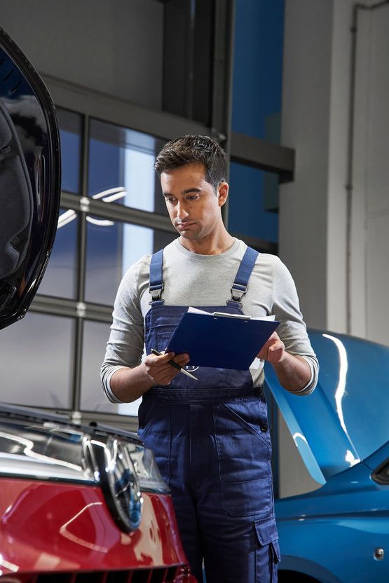 überprüft einen roten und einen blauen Volkswagen in einer Werkstatt. Die Volkswagen Werkstatt hat moderne Beleuchtung und große Fenster im Hintergrund.