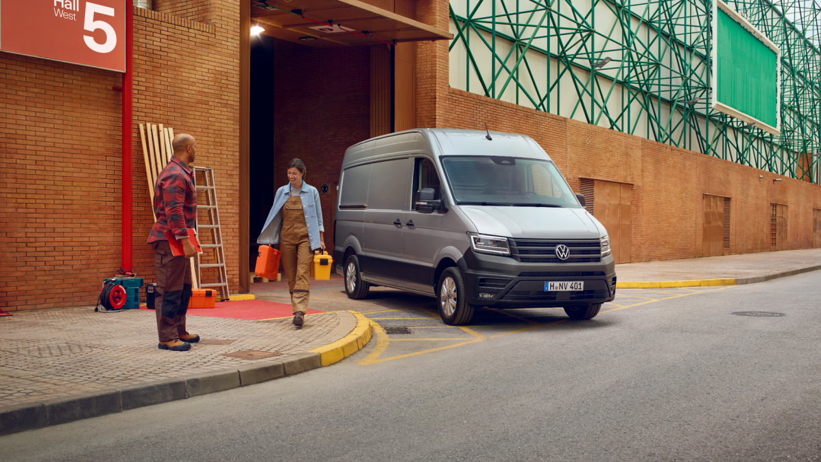 Zwei Handwerker neben einem silbernen Crafter Kastenwagen bei einer Werkshalle.