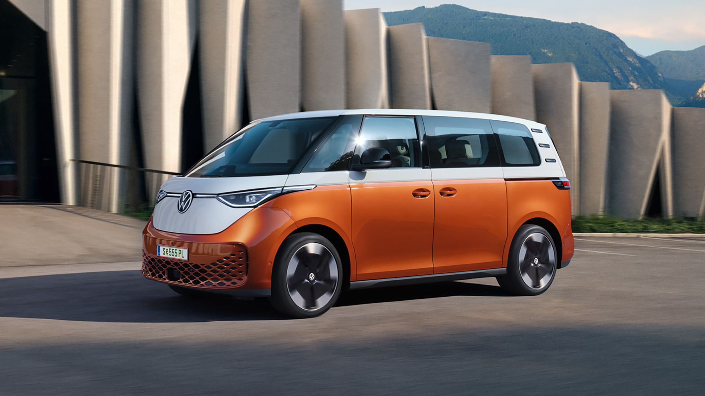 Der VW ID. Buzz steht vor einem modernen Gebäude mit Bergen im Hintergrund