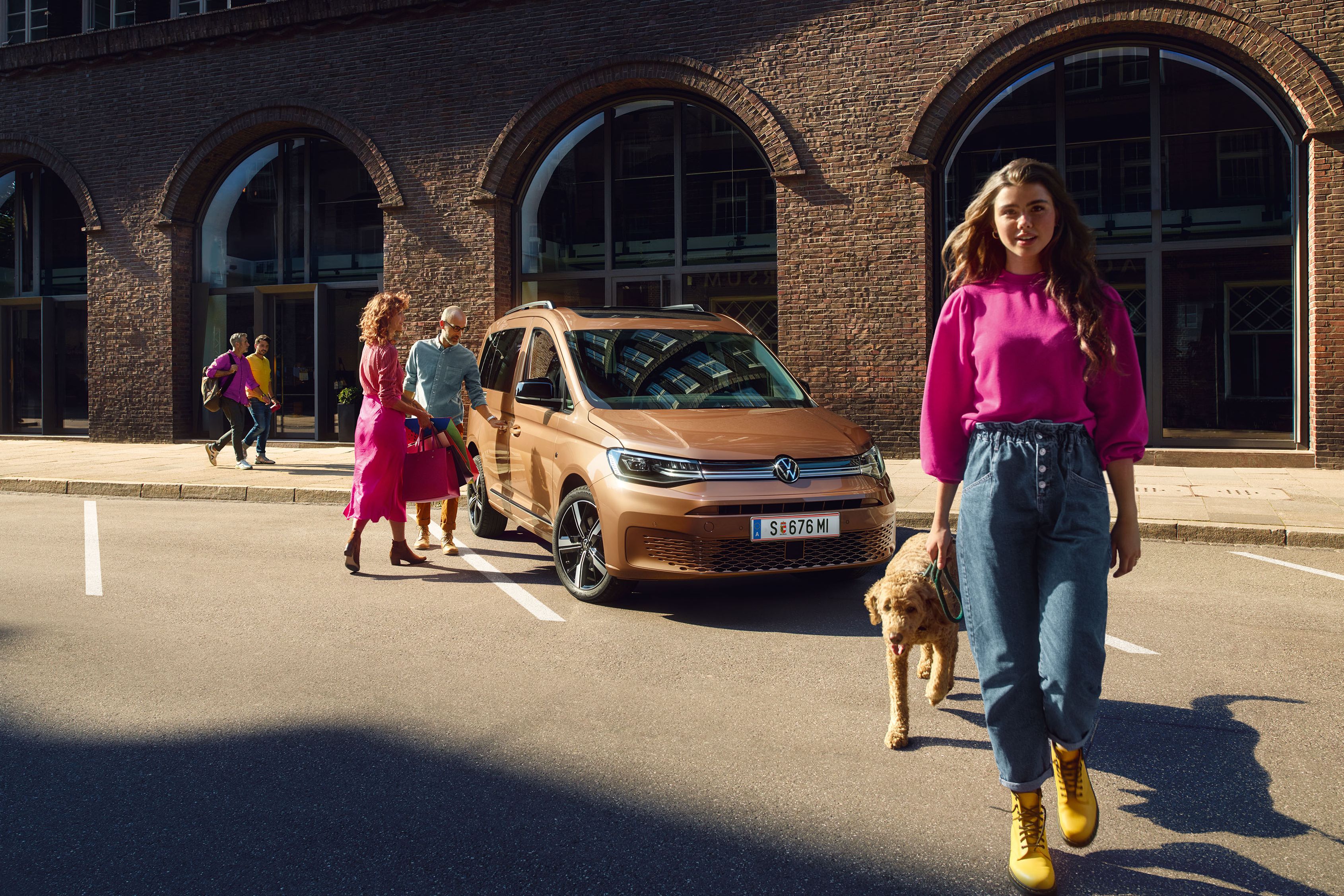 VW Caddy Cargo in Copper Bronze. Familie mit Hund stehen in der Nähe.
