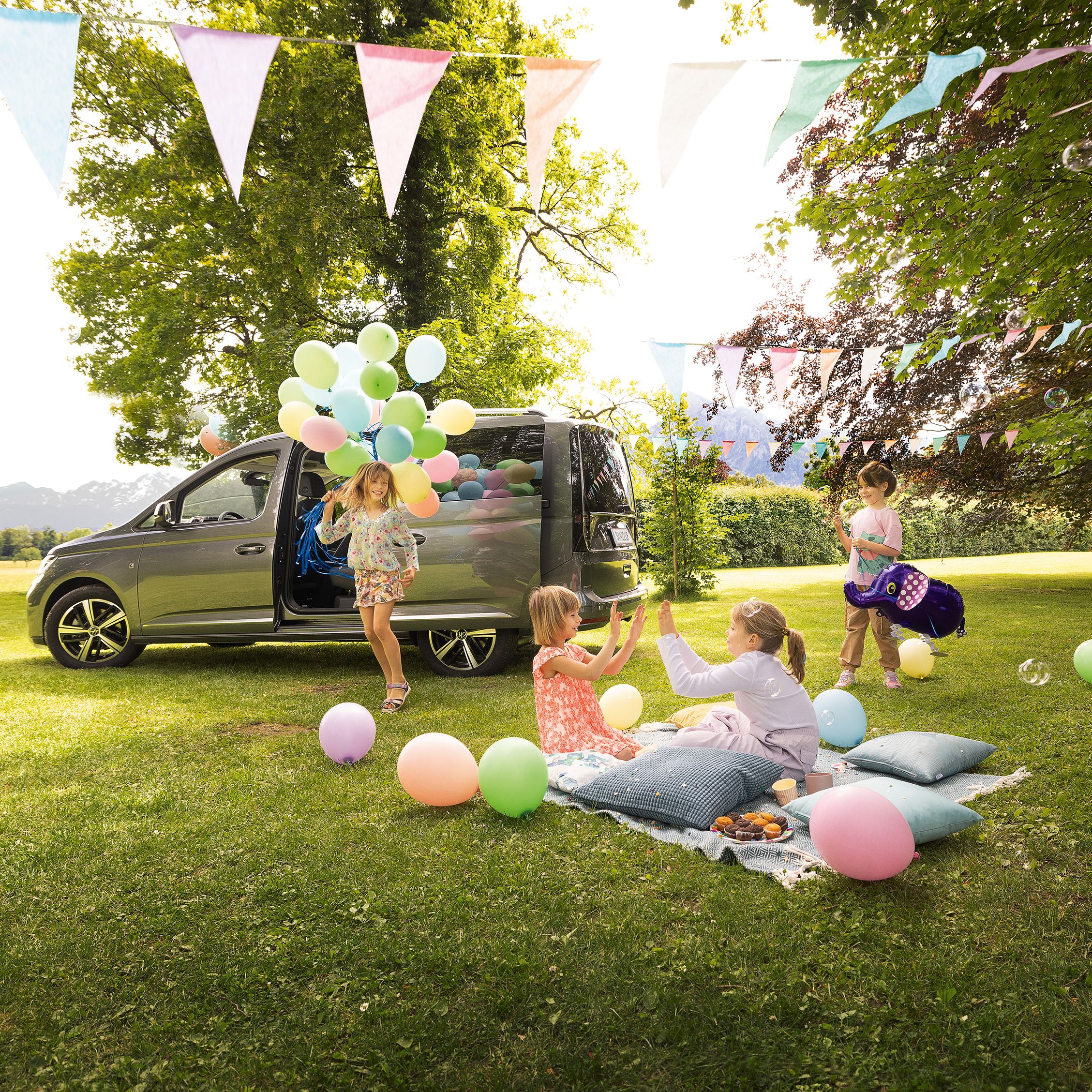 VW Caddy steht im Garten, Kinder spielen neben dem Fahrzeug und feiern Geburtstag