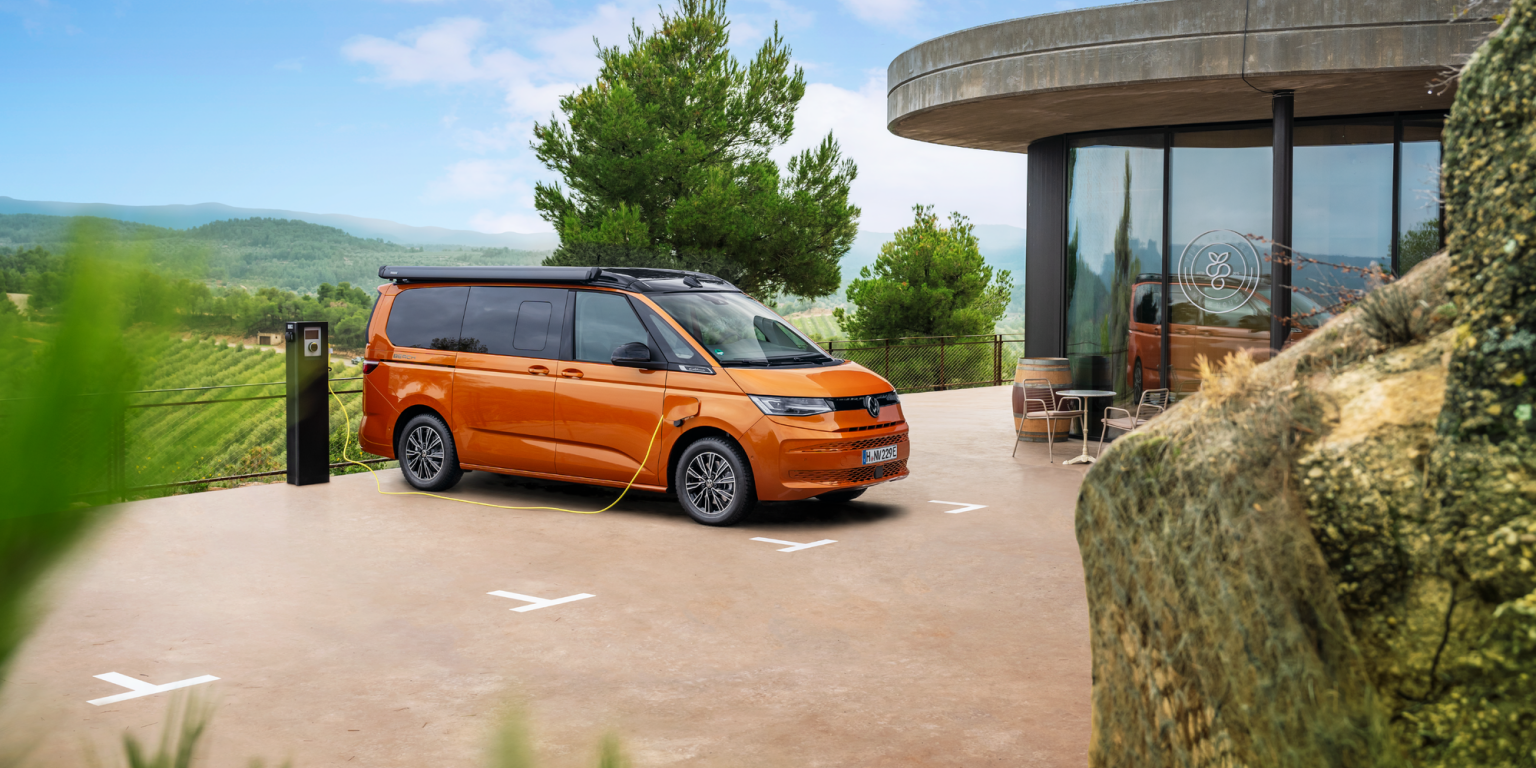 Ein oranger Volkswagen California beim Ladevorgang an einer Ladesäule.
