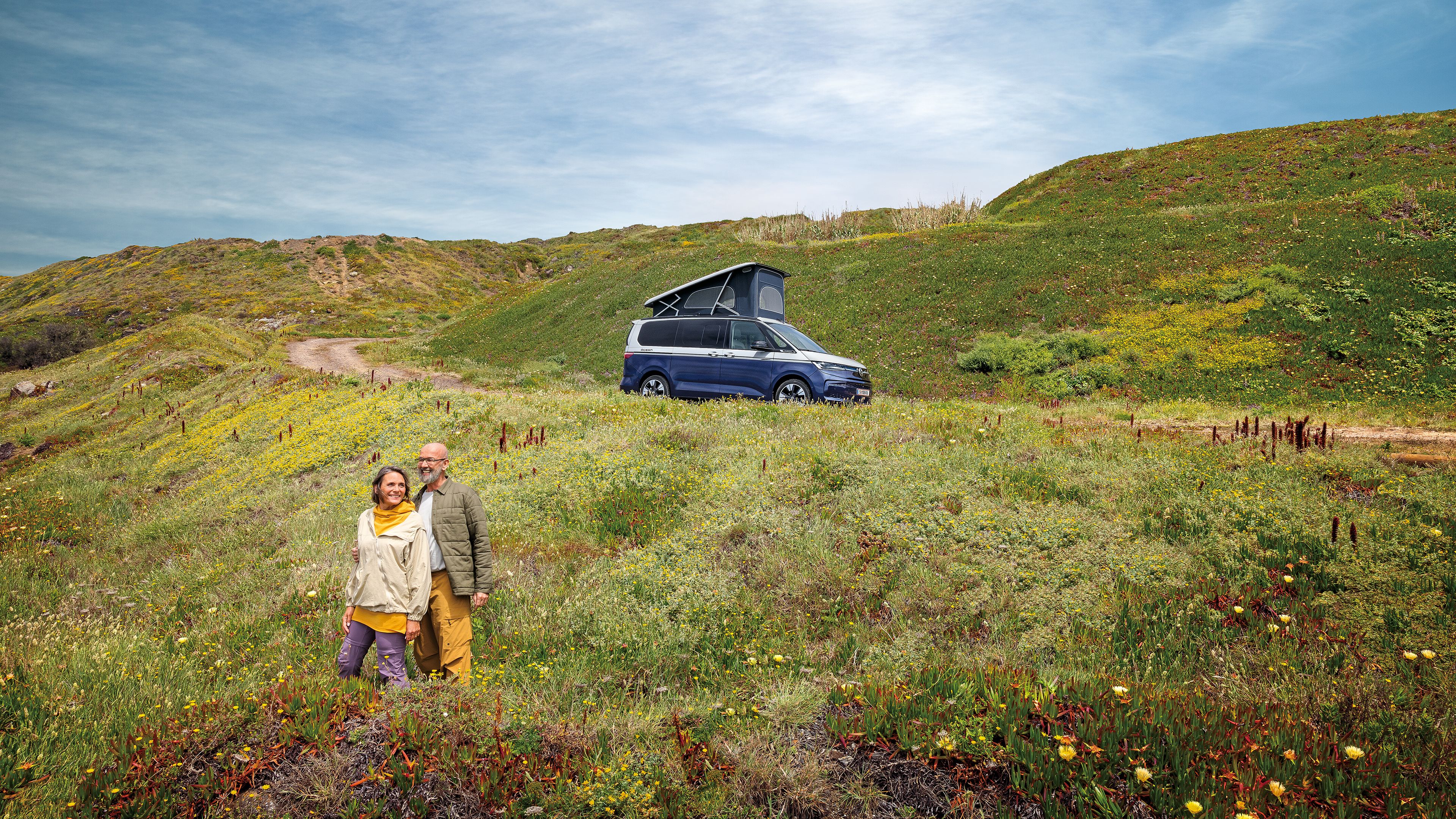 Ein VW California steht auf einer Schotterstraße am Meer