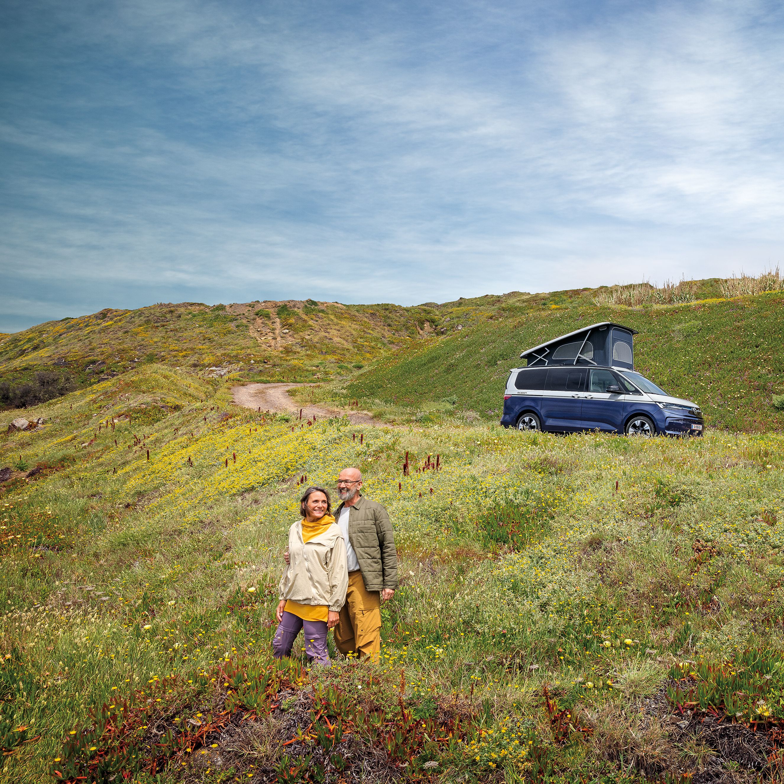 Ein VW California steht auf einer Schotterstraße am Meer