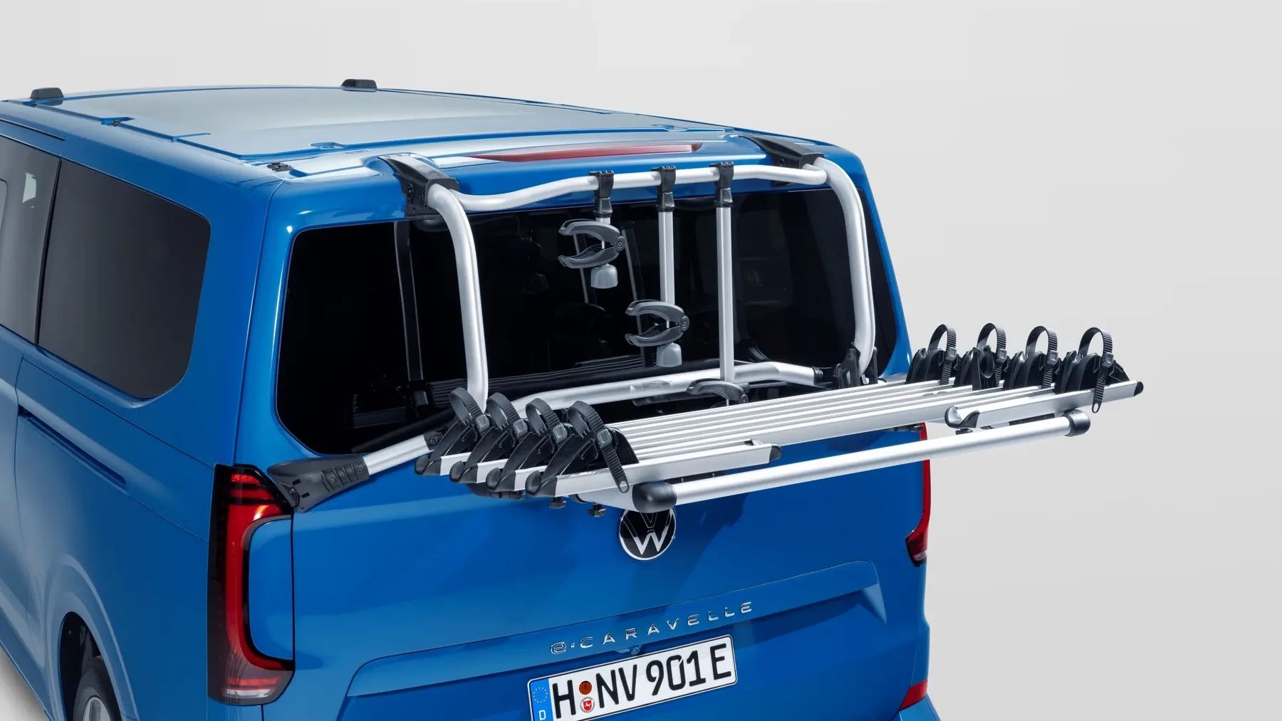 Heckansicht eines blauen Volkswagen Caravelle mit einem montierten Fahrradträger. Der silberne Träger ist aus Aluminium, nach hinten ausgeklappt und bietet mehrere Schienen für Fahrräder.