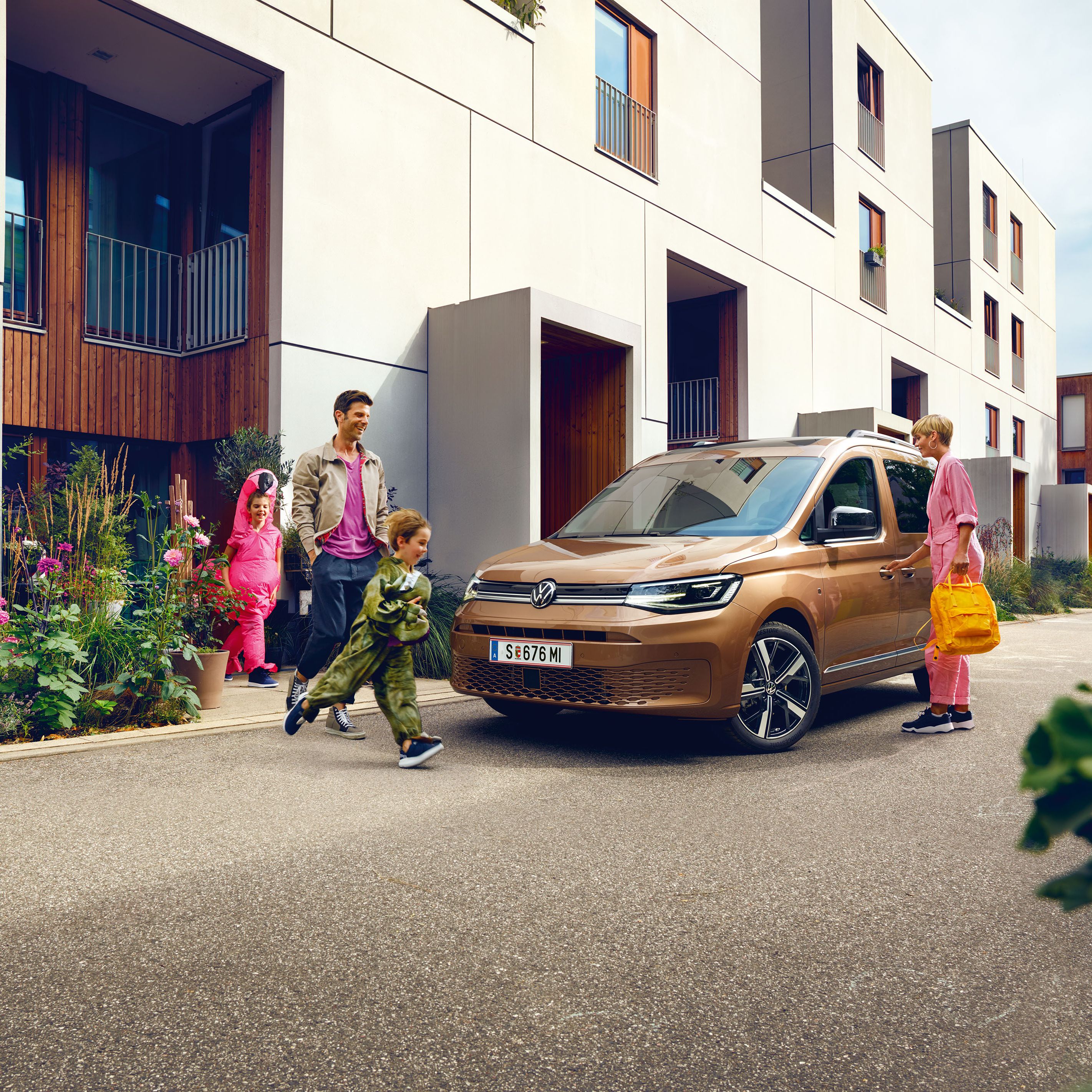 Eine junge Familie steigt vor der Wohnung in einen VW Caddy ein.