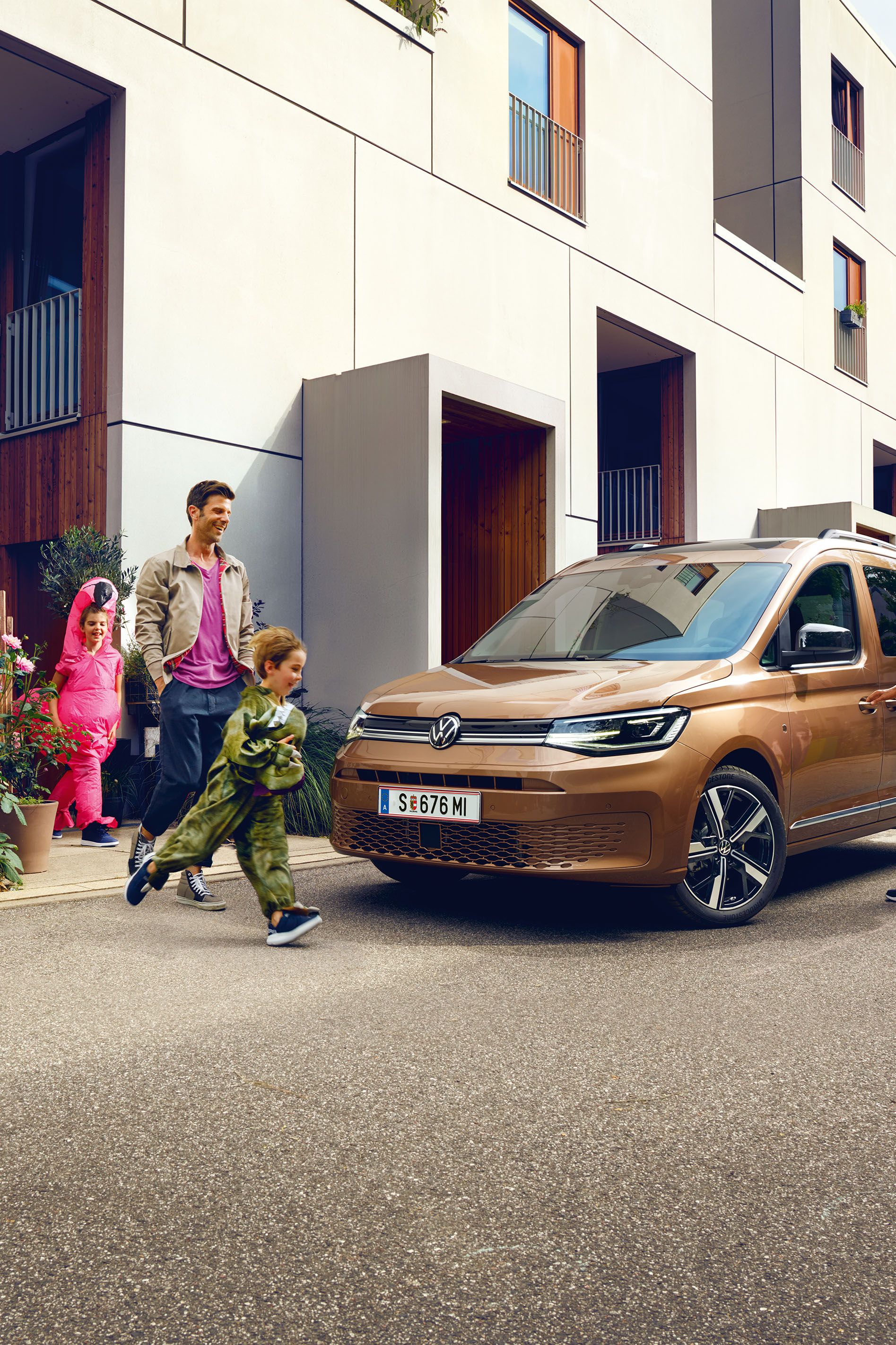 Eine junge Familie steigt vor der Wohnung in einen VW Caddy ein.
