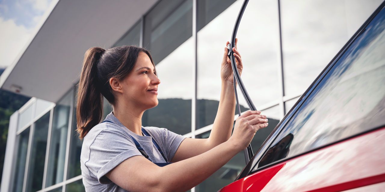 Eine Volkswagen Mechanikerin montiert Wischerblätter an einem Volkswagen.