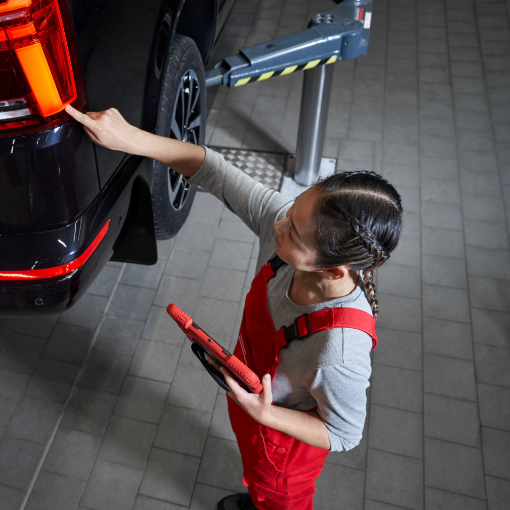 Eine VW Service Partnerin begutachtet die Heckleuchten eines VW Nutzfahrzeugs