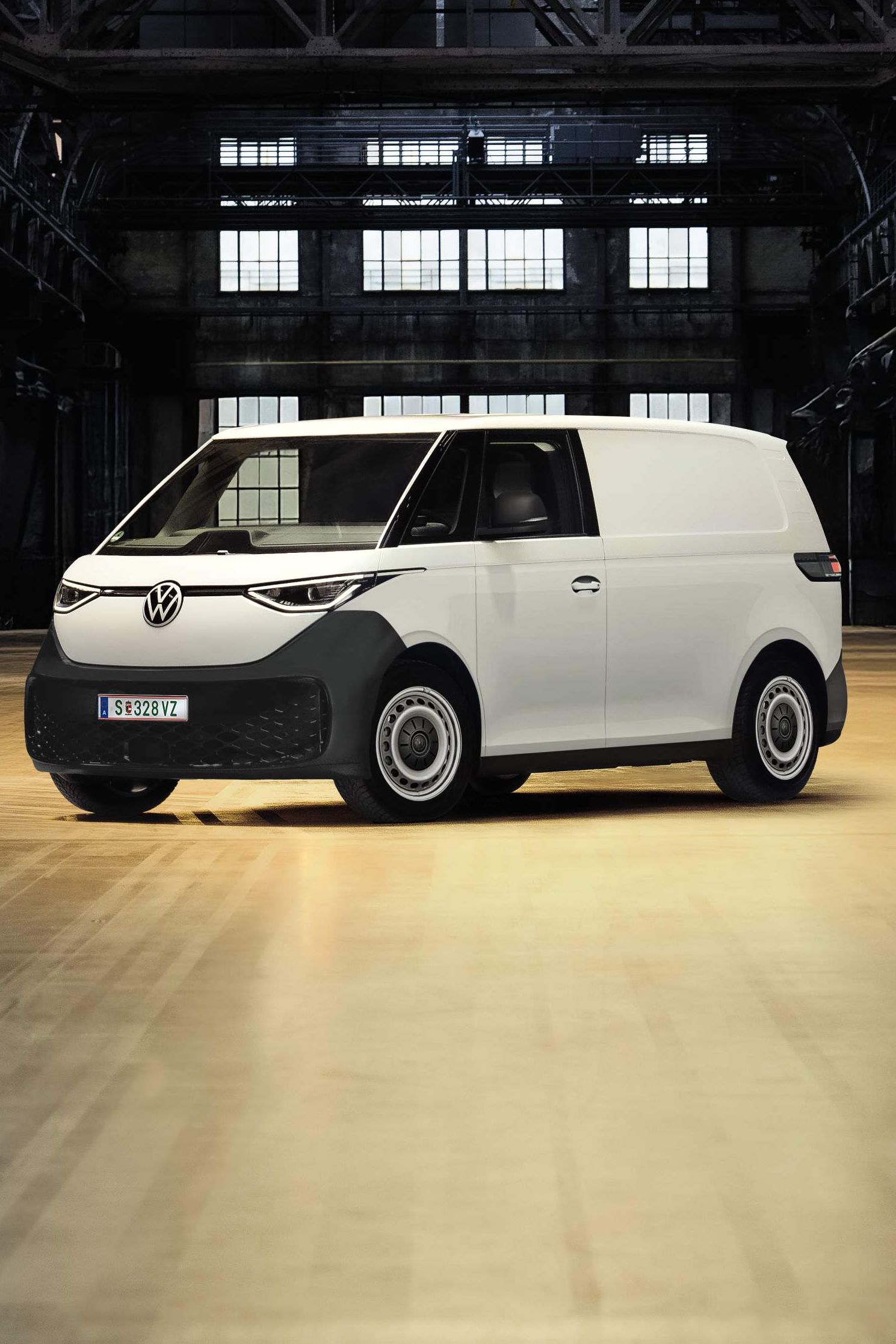 Ein weißer Lieferwagen steht allein in einer großen, dunklen Industriehalle. Die Umgebung ist leer und weist Metallstrukturen sowie Fenster im Hintergrund auf. Ein einzelner Scheinwerfer beleuchtet den Lieferwagen.