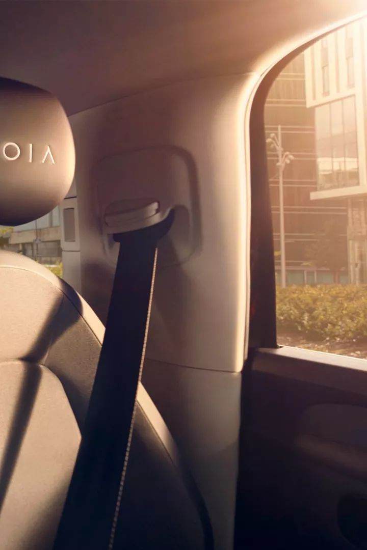 Ein Kind sitzt auf dem Rücksitz eines Autos und spielt auf einem Tablet, während ein Erwachsener neben ihm sitzt. Die Sitze haben einen schwarzen Bezug mit dem Logo "MOIA". Das Auto ist geräumig und von Tageslicht durchflutet.