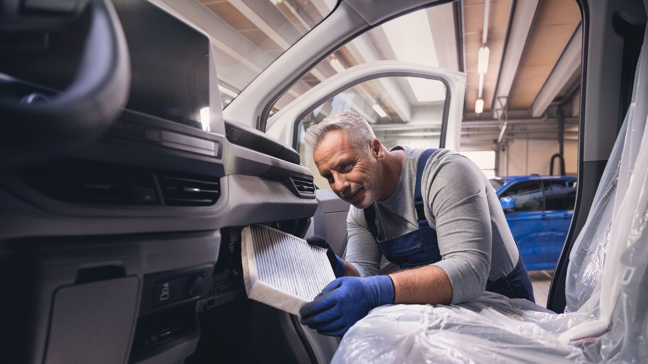 Ein Volkswagen Techniker wechselt den Filter einer Klimaanlage bei einem Volkswagen Nutzfahrzeug.