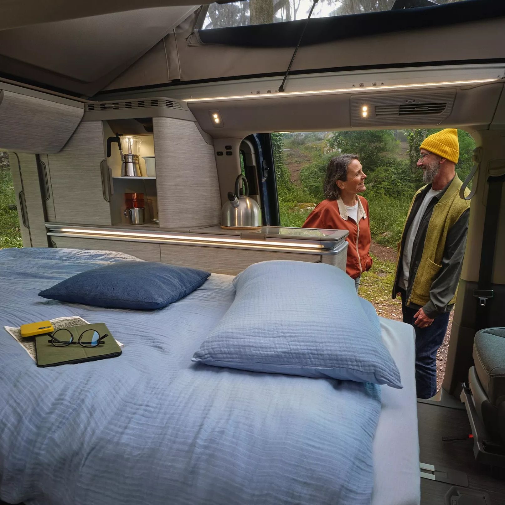 Der neue California Camper mit bezogenem Bett, gemütlicher Belichtung und 2 Personen unterhalten sich