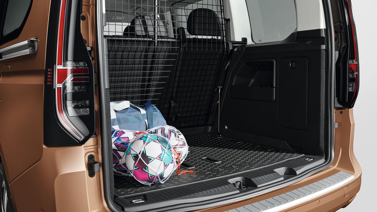 Offener Kofferraum eines Volkswagen Caddy mit Gittertrennwand zum Fahrgastraum. Auf dem gummierten Ladeboden liegen eine bunte Sporttasche und ein farbiges, geometrisch gemustertes Ballnetz.