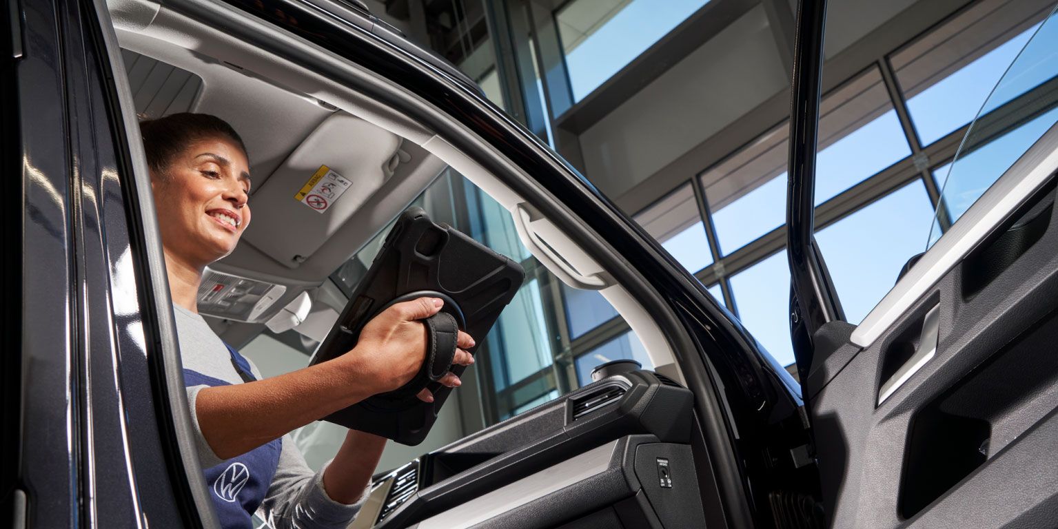 Eine Volkswagen Service Technikerin sitzt in einem Volkswagen Nutzfahrzeug und blickt auf ein Tablet.