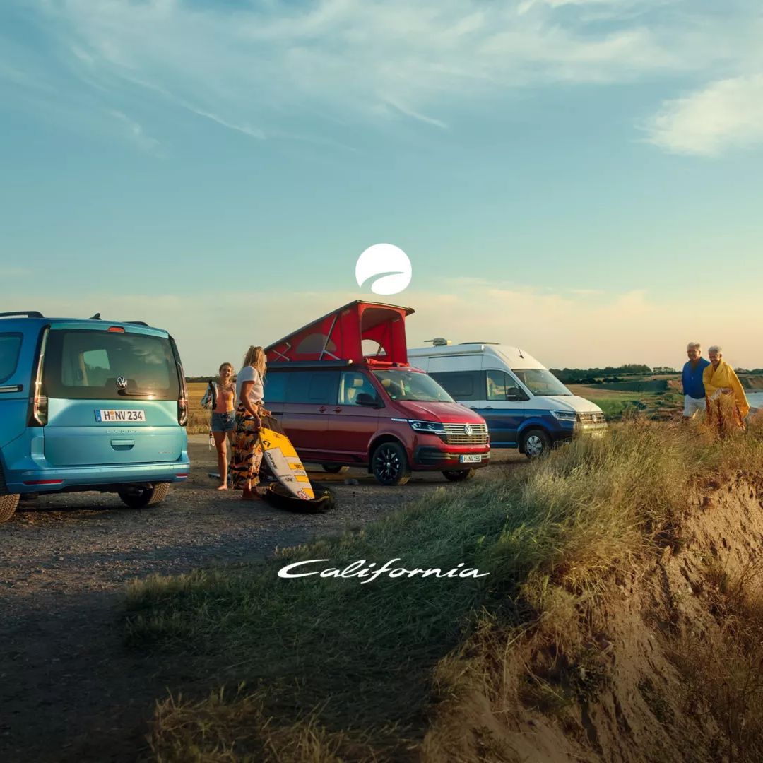 Vier verschiedene Volkswagen Camper stehen nebeneinander an der Küste, mit einer Familie, die das malerische Meerespanorama genießt. Ein Camper hat ein angehobenes Dach und eine Person scheint eine Surfbrett zu tragen. Die Szene ist bei Sonnenuntergang und strahlt eine entspannte Urlaubsstimmung aus.