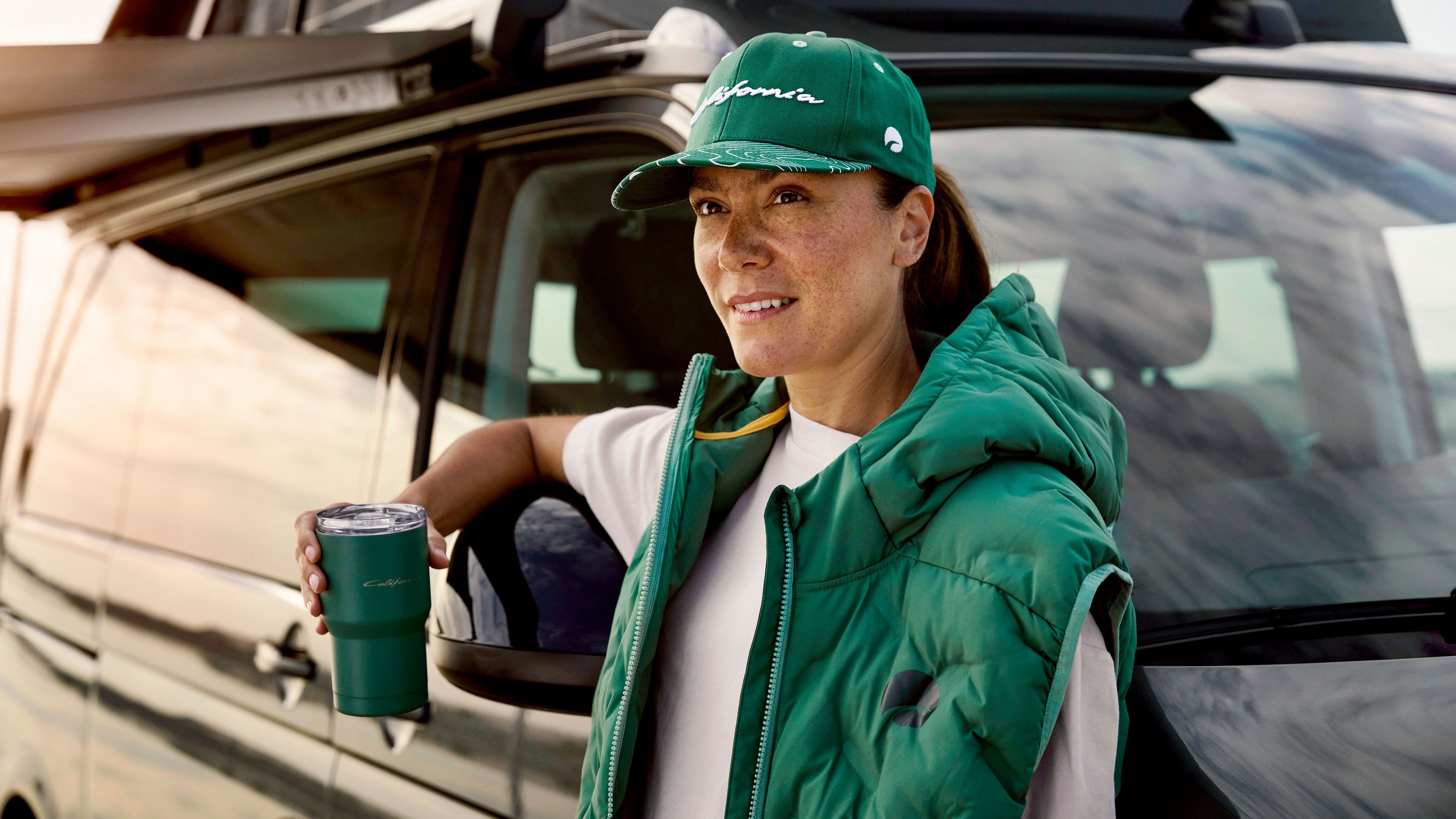 Eine Frau lehnt an einem Volkswagen California und blickt in die Ferne.