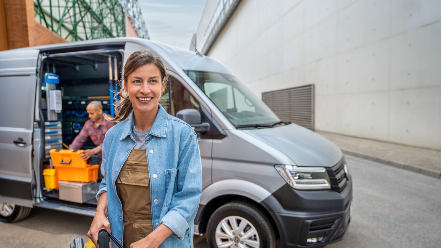 Eine Frau vor einem silbernen Crafter Kastenwagen, ein Mann kniet auf der Ladefläche.