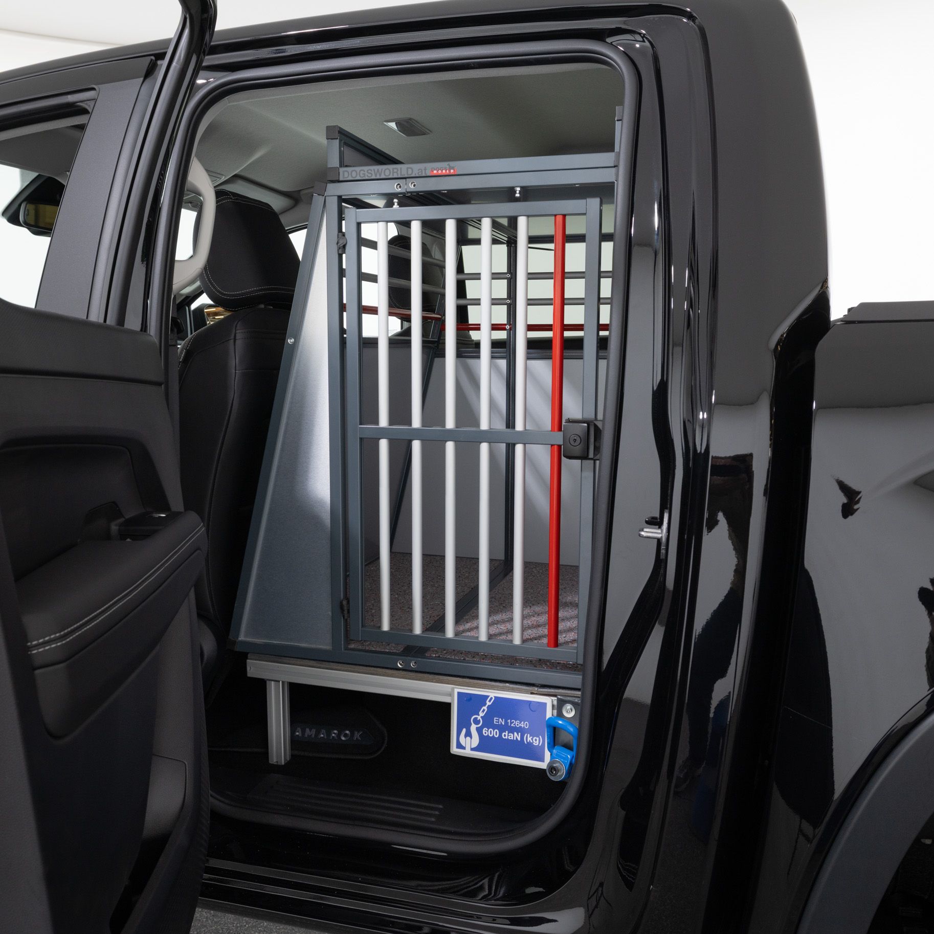 Eine Rückbank eines schwarzen Autos wurde ausgebaut und durch einen Tierkäfig ersetzt. Der Käfig befindet sich direkt hinter dem Fahrersitz und ist durch eine Tür mit Gitterstäben zugänglich. Außen ist ein Schild sichtbar, auf dem ein Hund abgebildet ist.