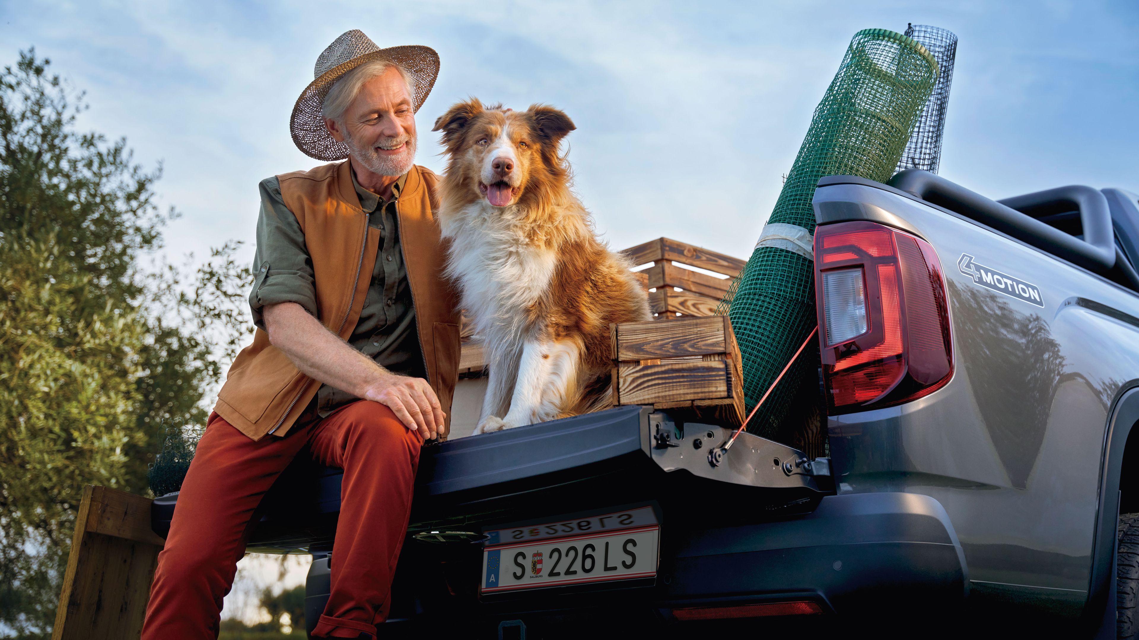 Ein Mann sitzt mit seinem Hund auf der Ladefläche eines Volkswagen Amarok.