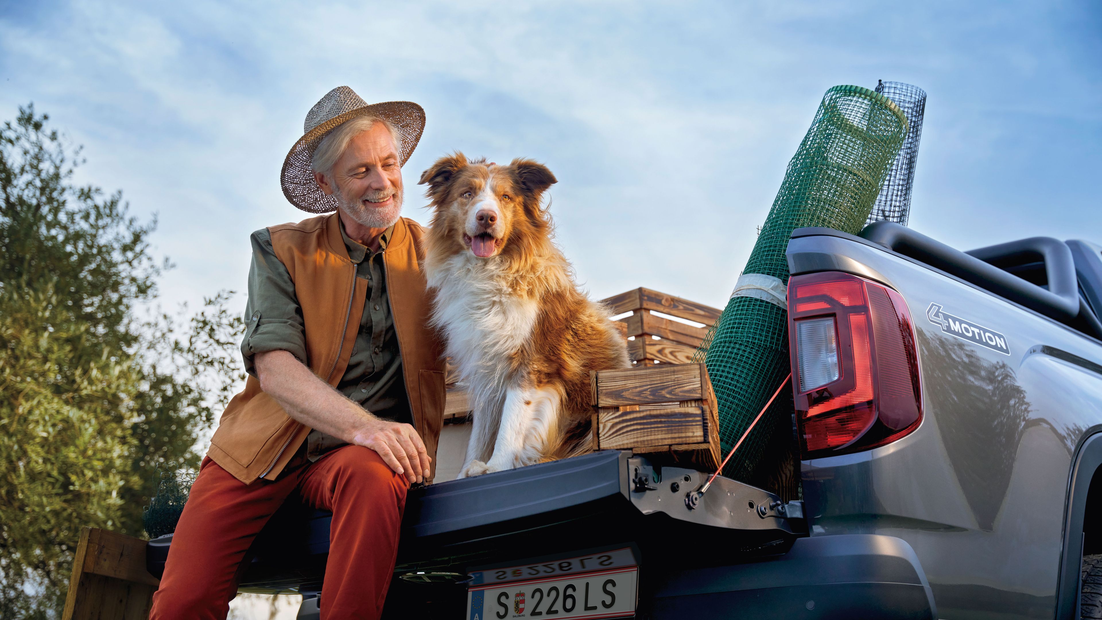 Ein Mann sitzt mit seinem Hund auf der Ladefläche eines Volkswagen Amarok.