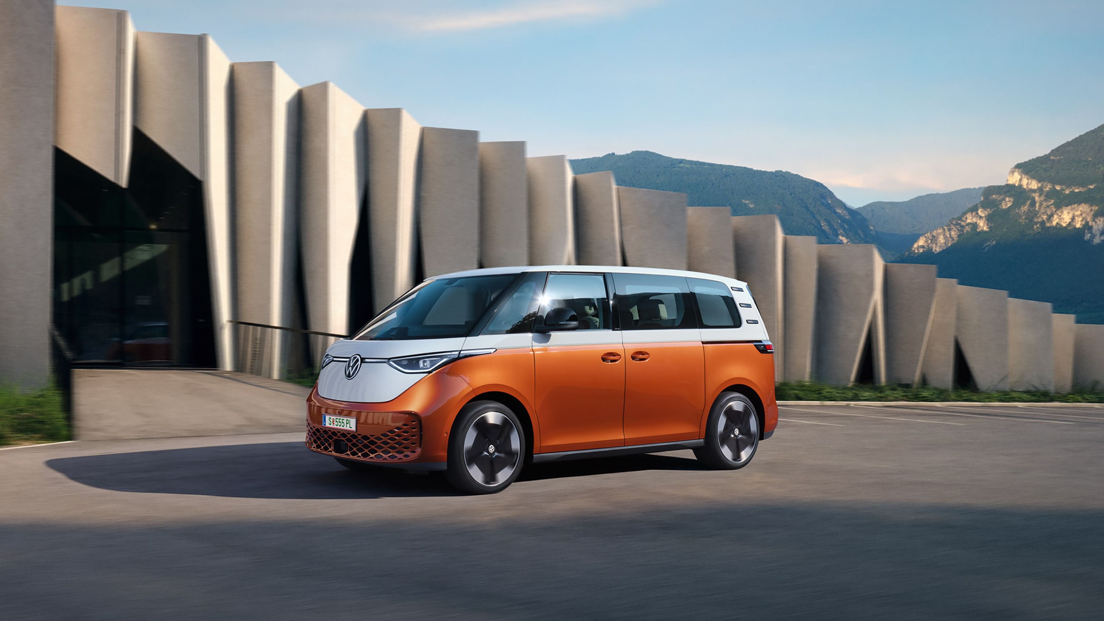 Der VW ID. Buzz steht vor einem modernen Gebäude mit Bergen im Hintergrund