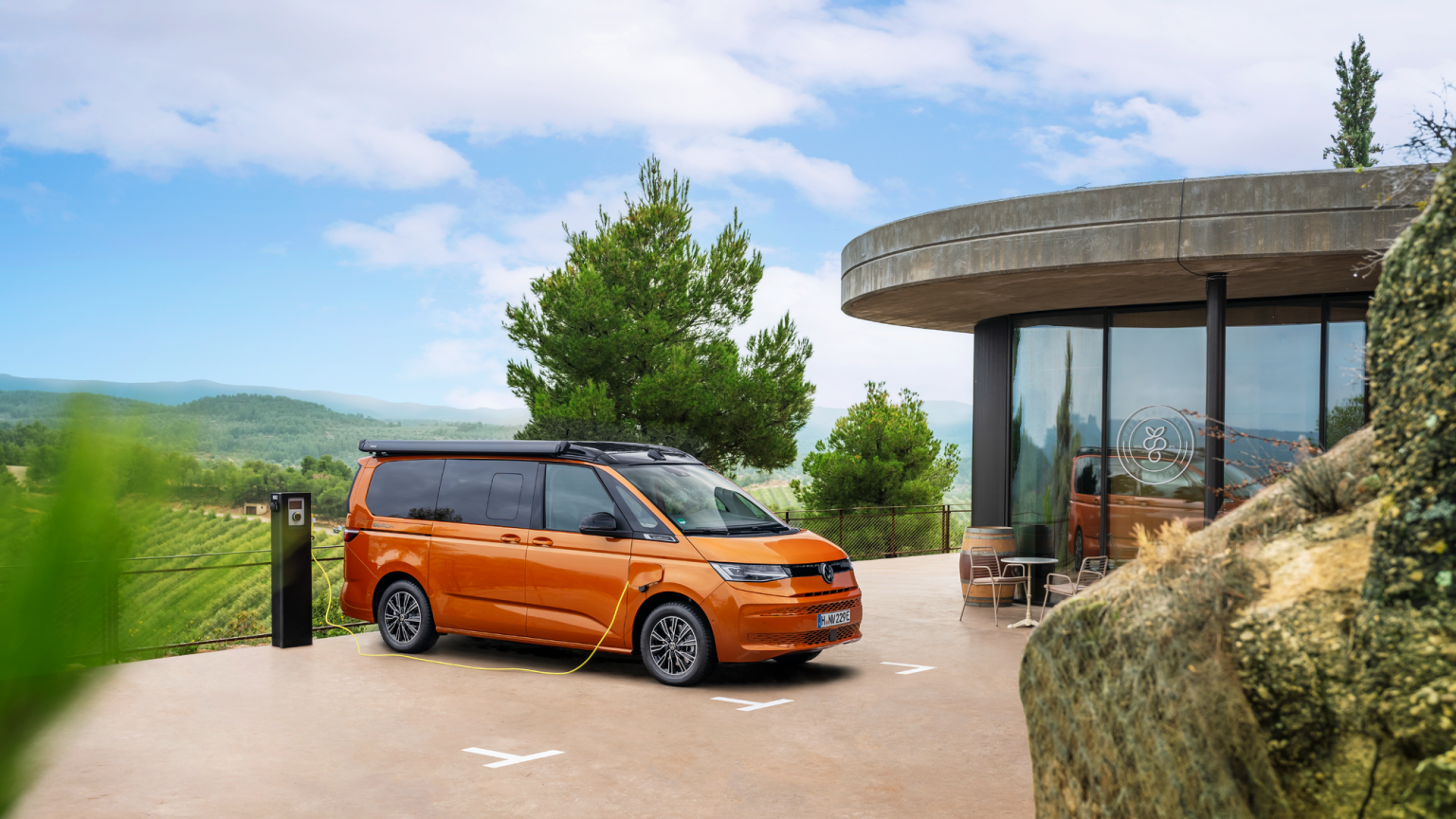 Ein oranger Volkswagen California beim Ladevorgang an einer Ladesäule.
