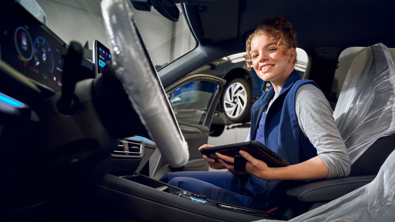 Eine Volkswagen Technikerin sitzt mit ihrem Tablet in einem Volkswagen Tiguan
