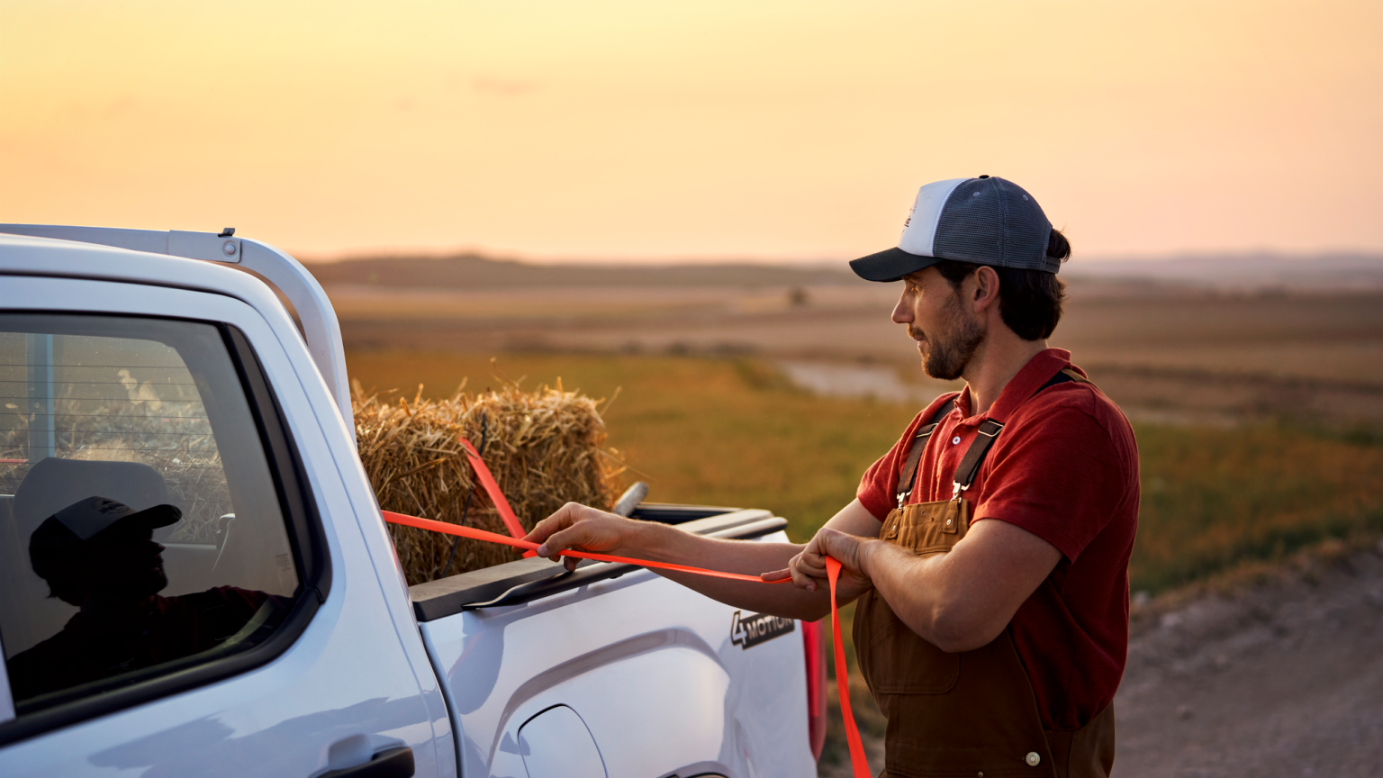 Ein Mann zurrt einen Strohballen an der Ladefläche eines Volkswagen Amarok fest.