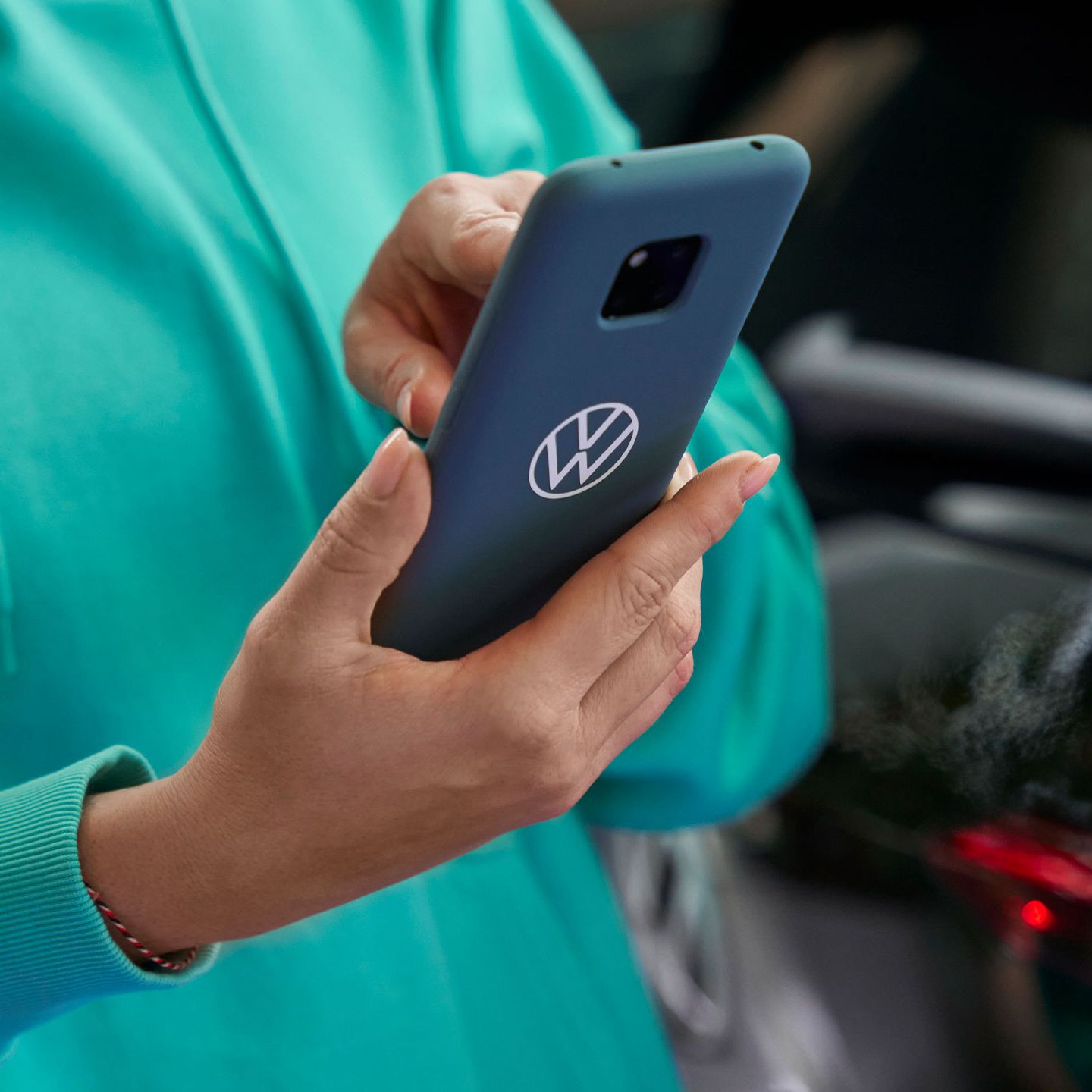 Eine Frau tippt in ihr Smartphone. Auf der blauen Schutzhülle ist das Volkswagen Logo abgebildet.