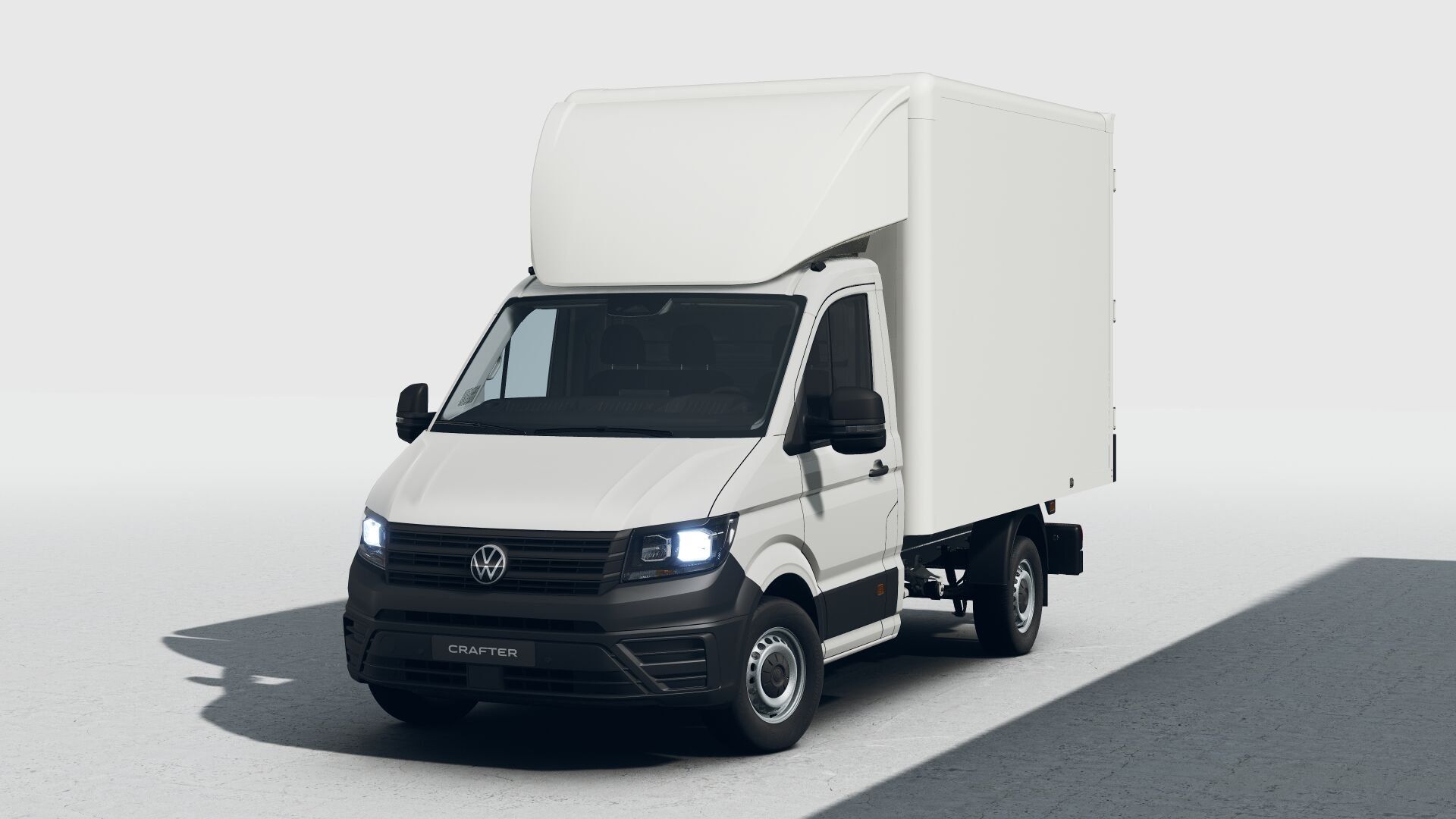 Ein weißer Volkswagen Crafter Transporter steht vor einem hellen Hintergrund. Das Fahrzeug ist ein Kastenwagen mit einem hohen, rechteckigen Laderaum. Die Frontscheinwerfer des Transporters sind eingeschaltet.
