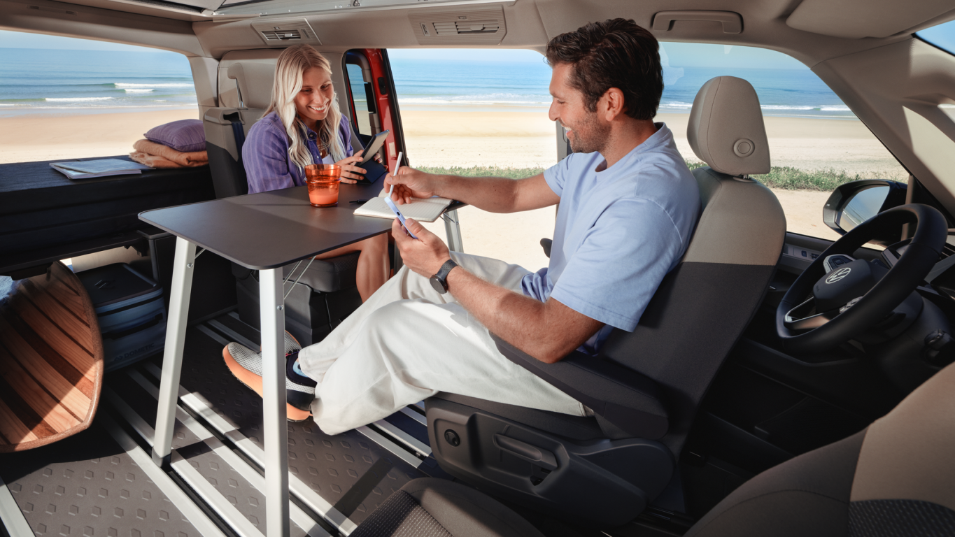 Ein Mann und eine Frau sitzen in einem Volkswagen California an ihrem Tisch.