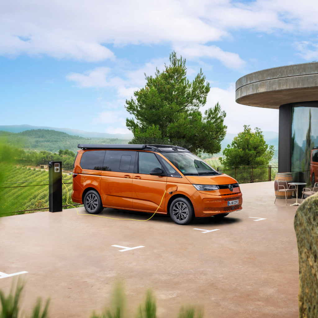 Ein oranger Volkswagen California beim Ladevorgang an einer Ladesäule.