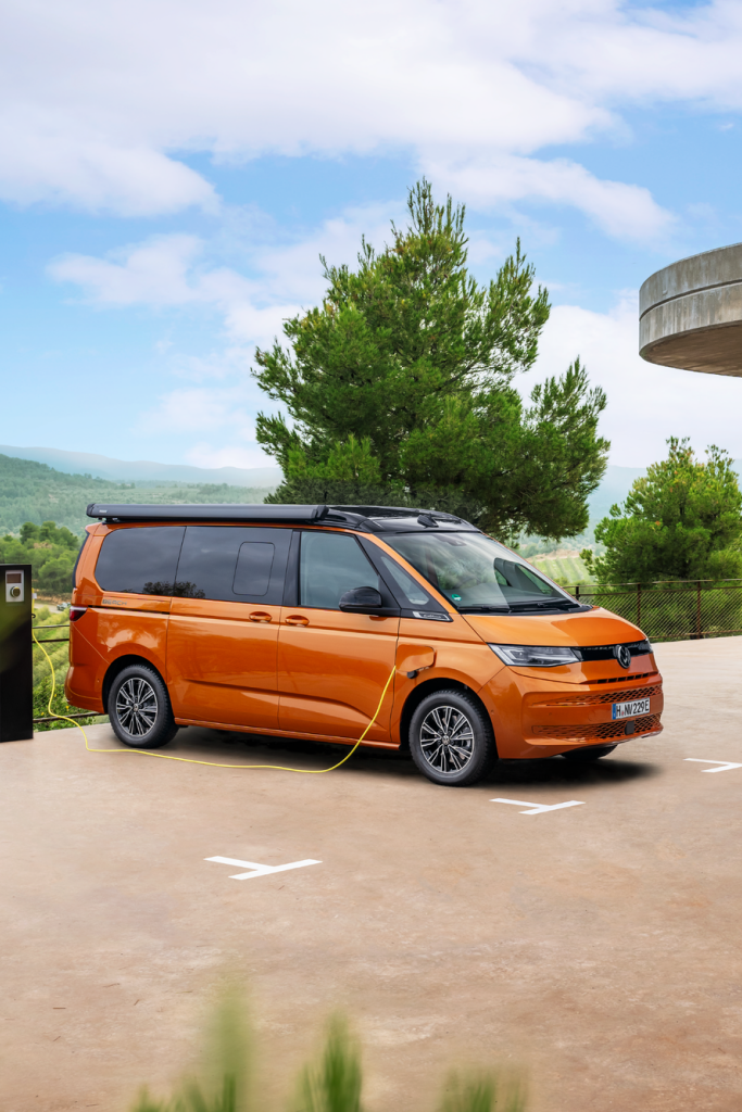 Ein oranger Volkswagen California beim Ladevorgang an einer Ladesäule.