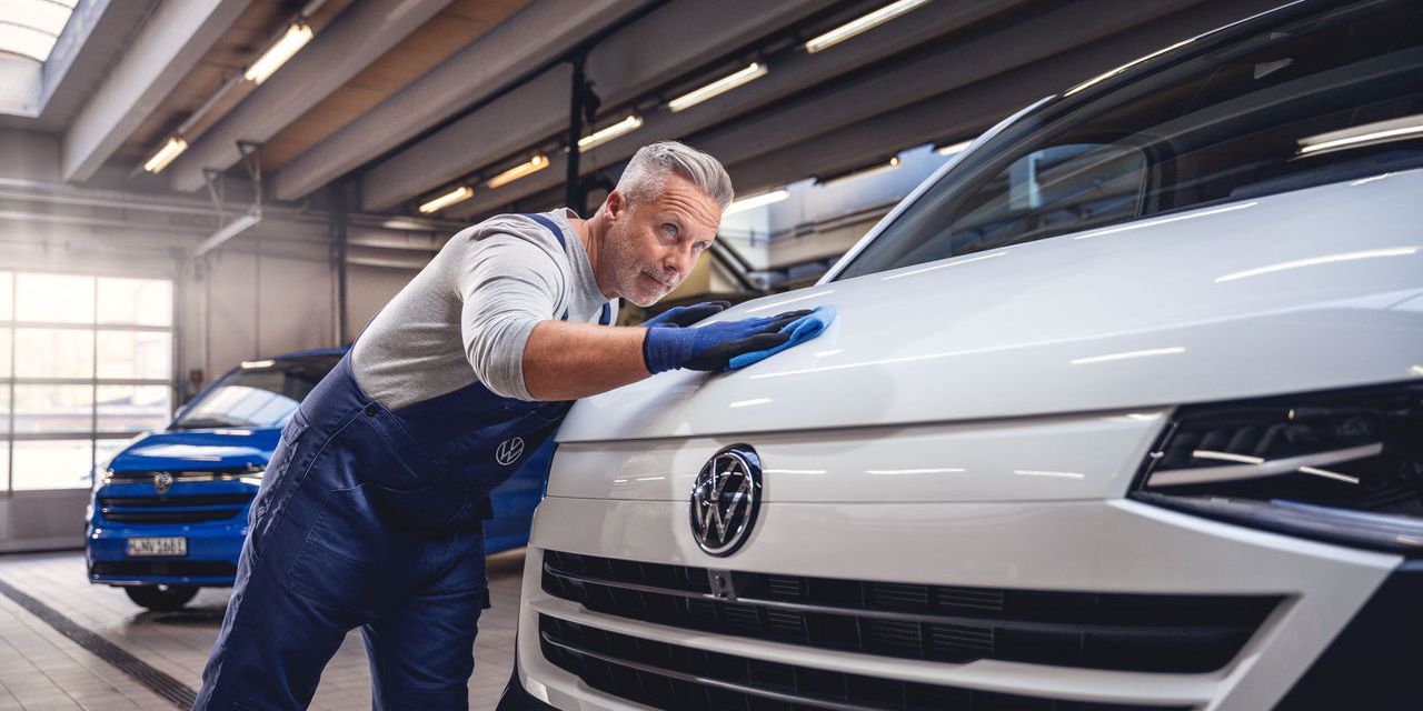Ein Volkswagentechniker poliert den Lack eines Volkswagen Nutzfahrzeugs mit einem Tuch.
