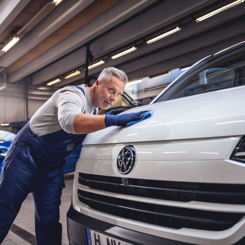 Ein Volkswagentechniker poliert den Lack eines Volkswagen Nutzfahrzeugs mit einem Tuch.