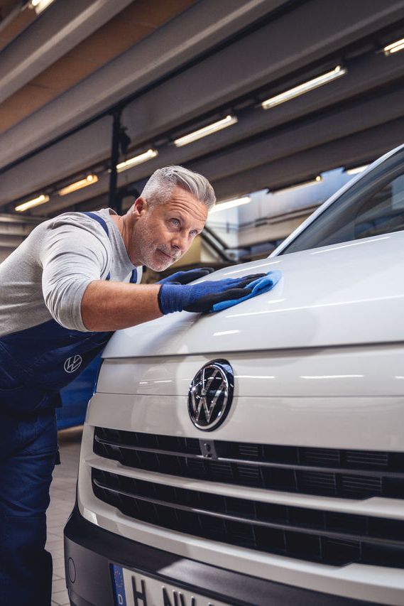 Ein Volkswagentechniker poliert den Lack eines Volkswagen Nutzfahrzeugs mit einem Tuch.