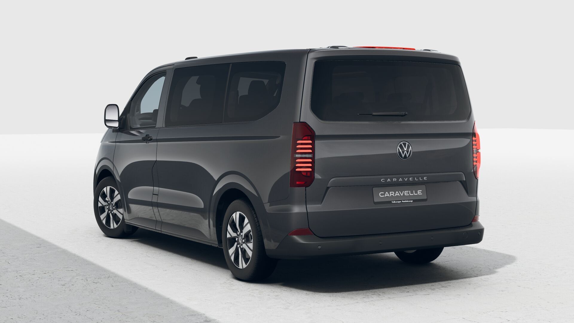 Ein grauer VW Caravelle steht auf einem Parkplatz. Das Heck des Fahrzeugs ist prominent sichtbar. Der Kleinbus hat getönte Scheiben und moderne LED-Rückleuchten.