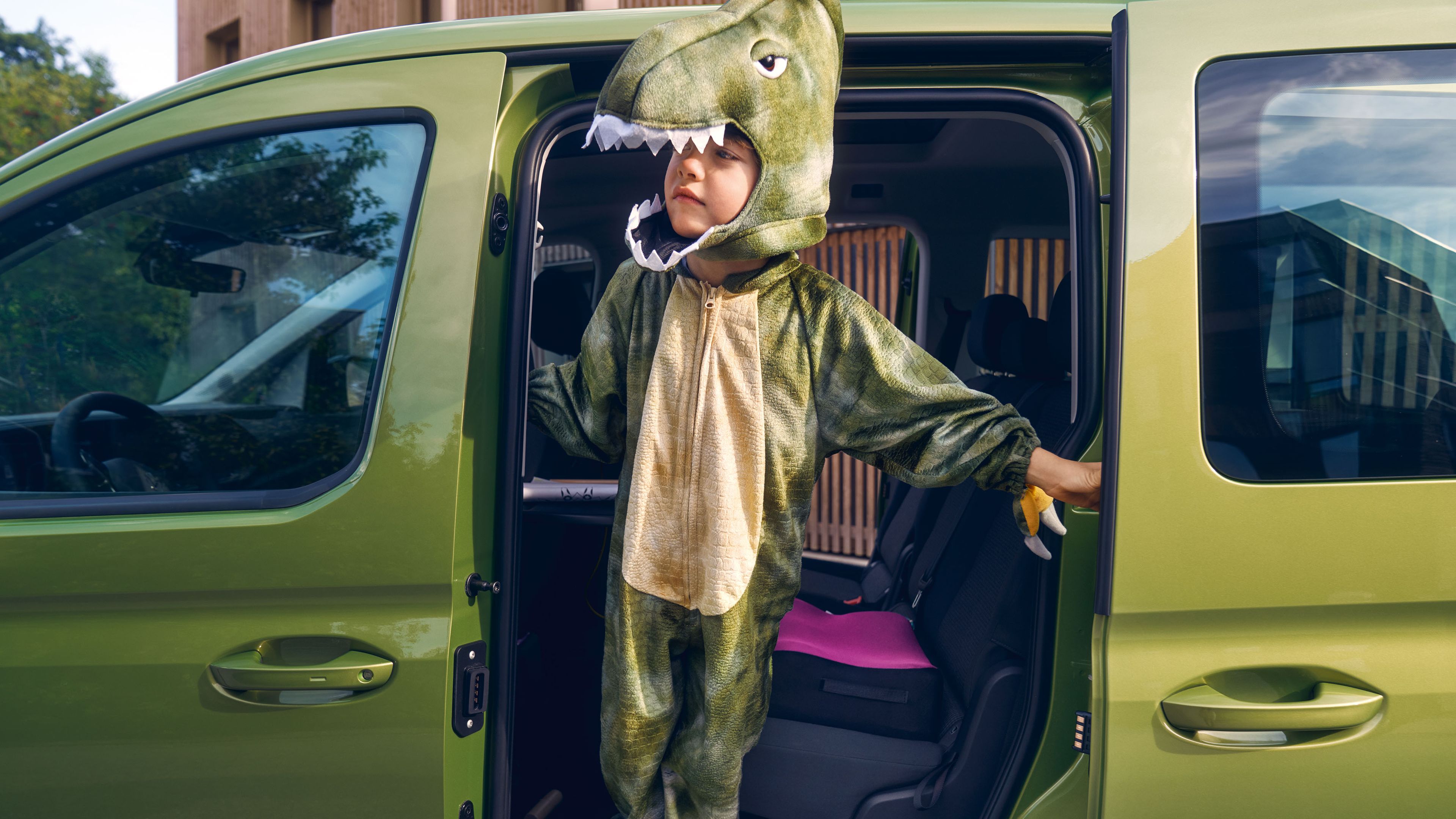 Ein Kind - als Krokodil verkleidet - lehnt sich aus der Tür eines grünen VW Caddys