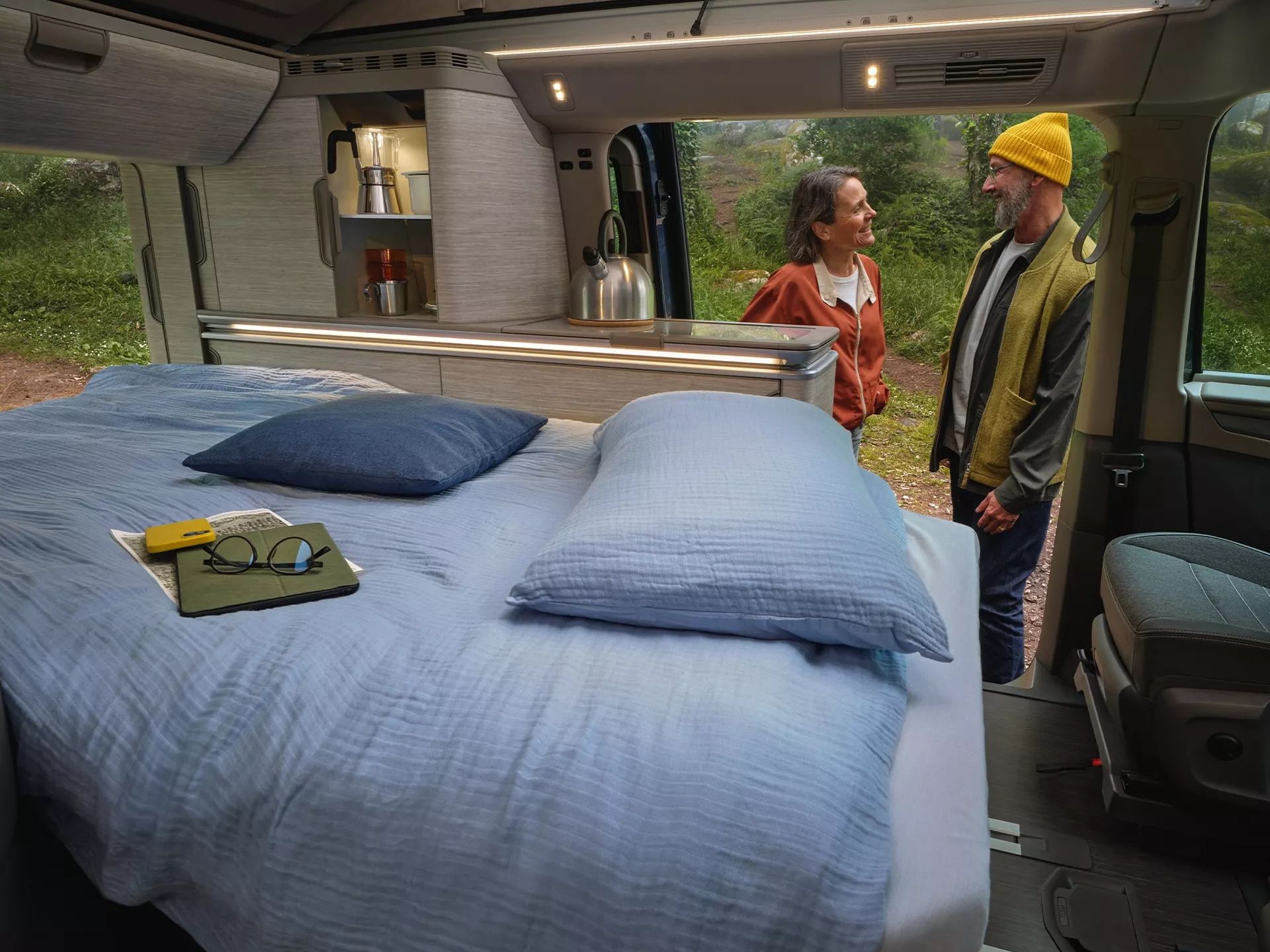 Der neue California Camper mit bezogenem Bett, gemütlicher Belichtung und 2 Personen unterhalten sich