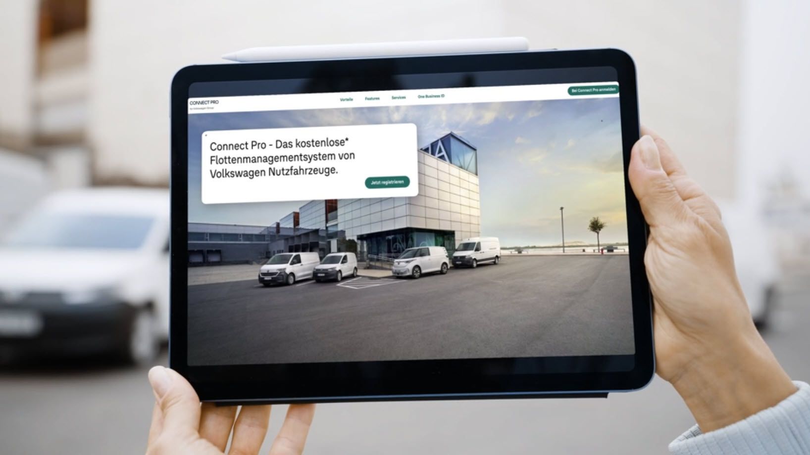 Eine Person hält ein Tablet, auf dem die Website "Volkswagen Nutzfahrzeuge" angezeigt wird. Der Bildschirm zeigt mehrere geparkte Lieferwagen vor einem modernen Gebäude. Die Seite bewirbt das Flottenmanagementsystem Connect Pro.