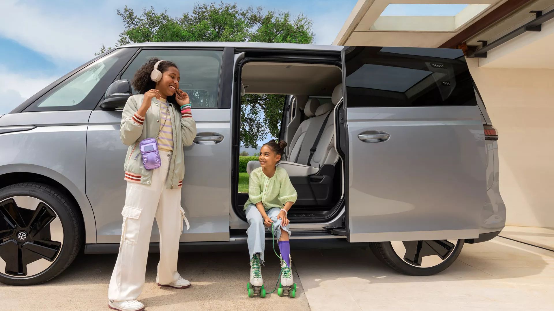Seitenansicht silberner ID. Buzz mit geöffneter Schiebetüre, zwei Kinder daneben