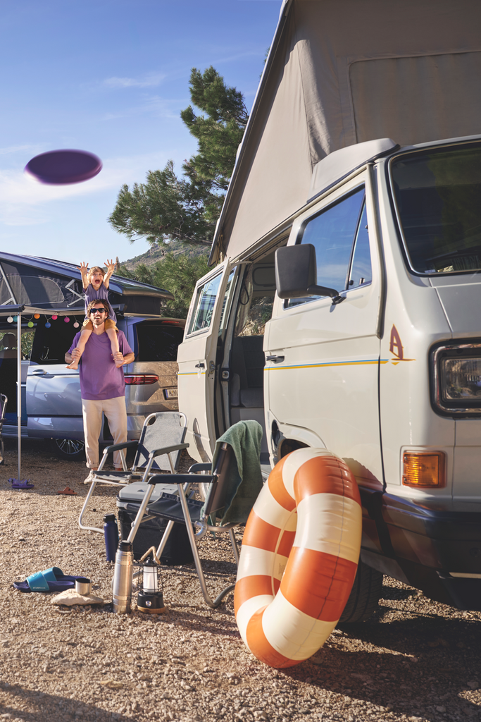 Eine Familie spielt auf einem Campingplatz, im Hintergrund ist ein Volkswagen California zu sehen.