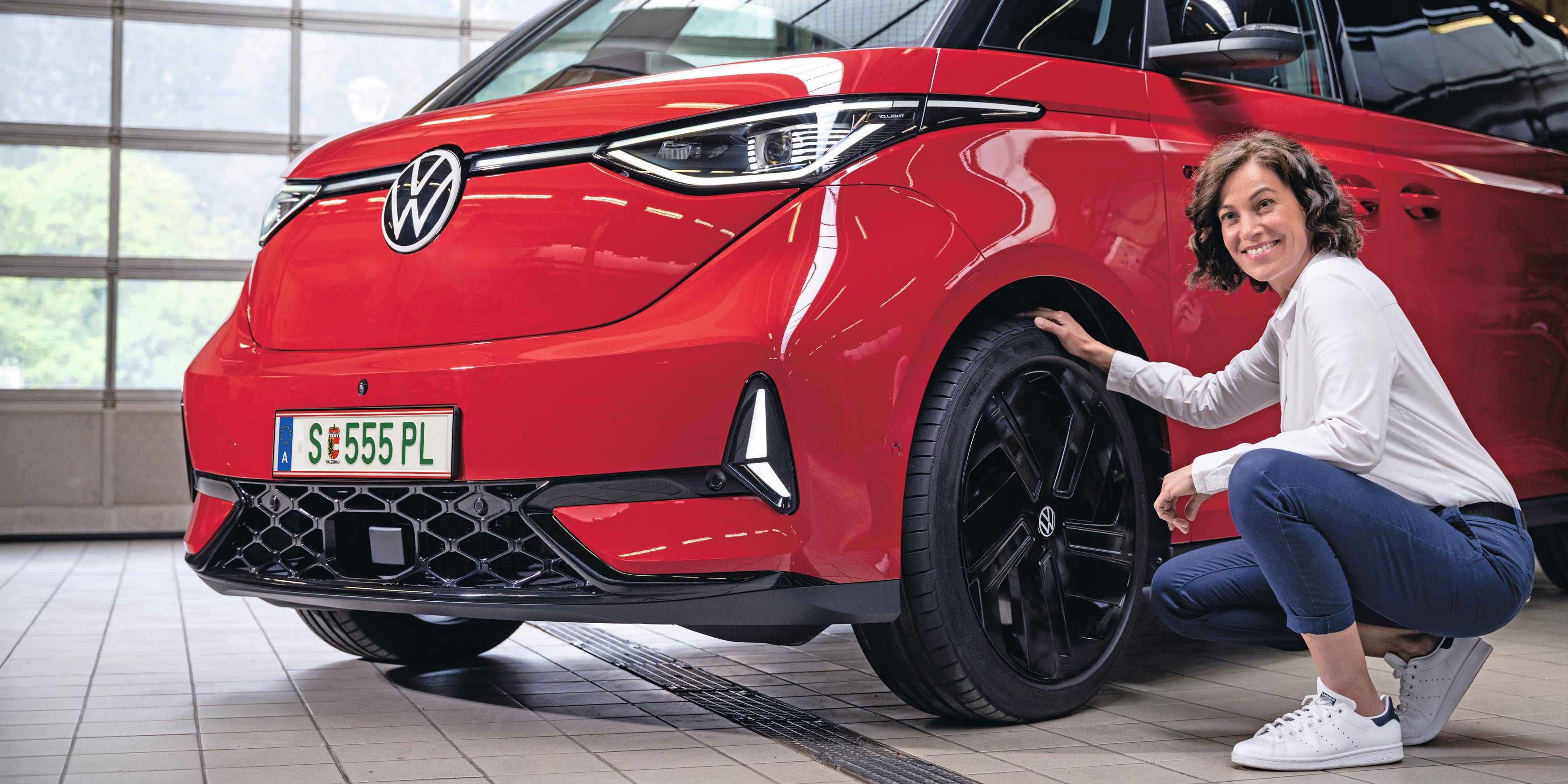 Ein Frau lächelnd in der Hocke vor einem roten Volkswagen ID. Buzz.