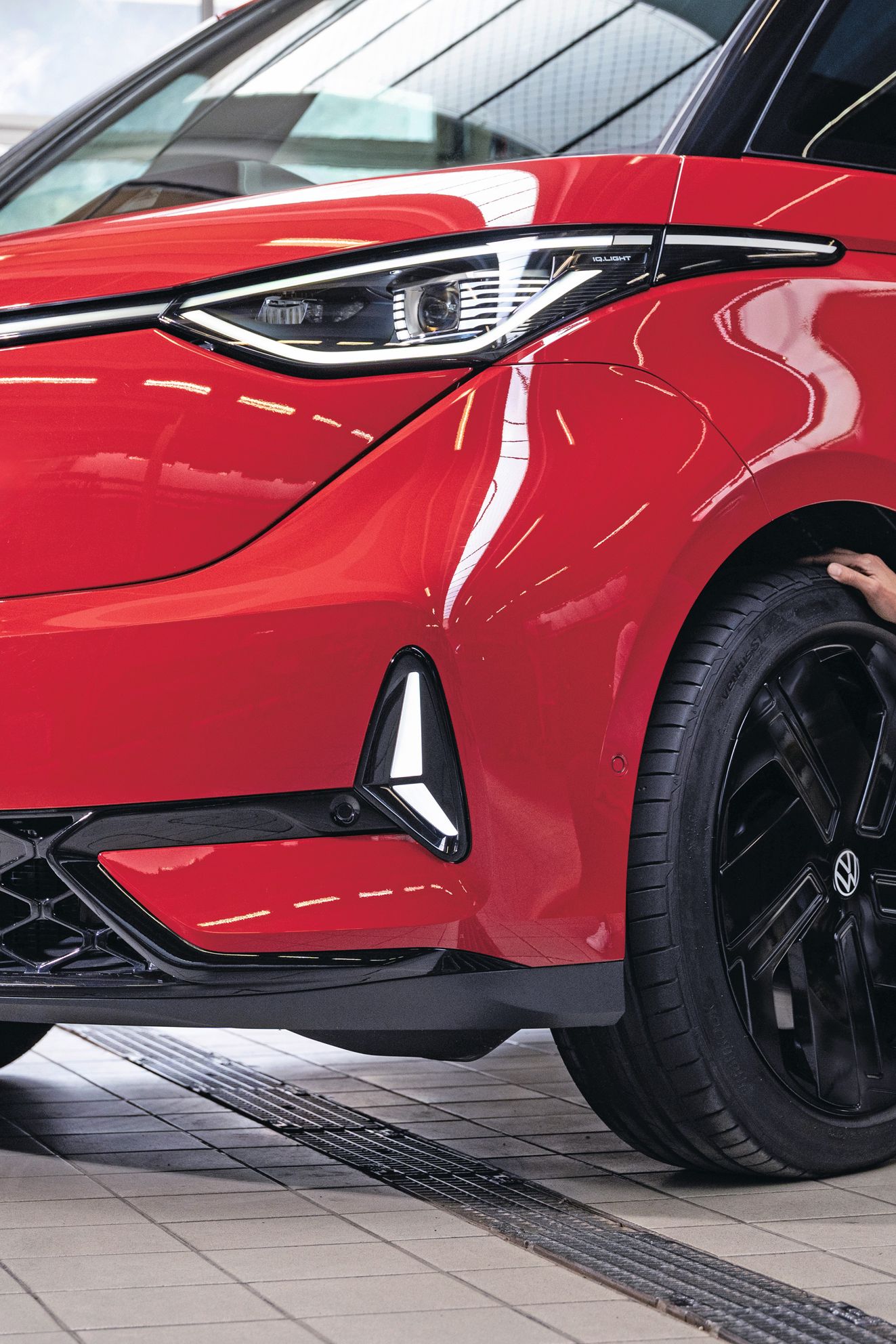 Ein Frau lächelnd in der Hocke vor einem roten Volkswagen ID. Buzz.