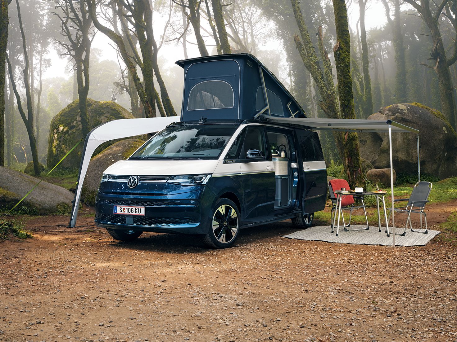 New California steht mit ausgeklapptem Dach und ausgefahrener Marquise in einem Wald, Campingstühle stehen unter der Marquise