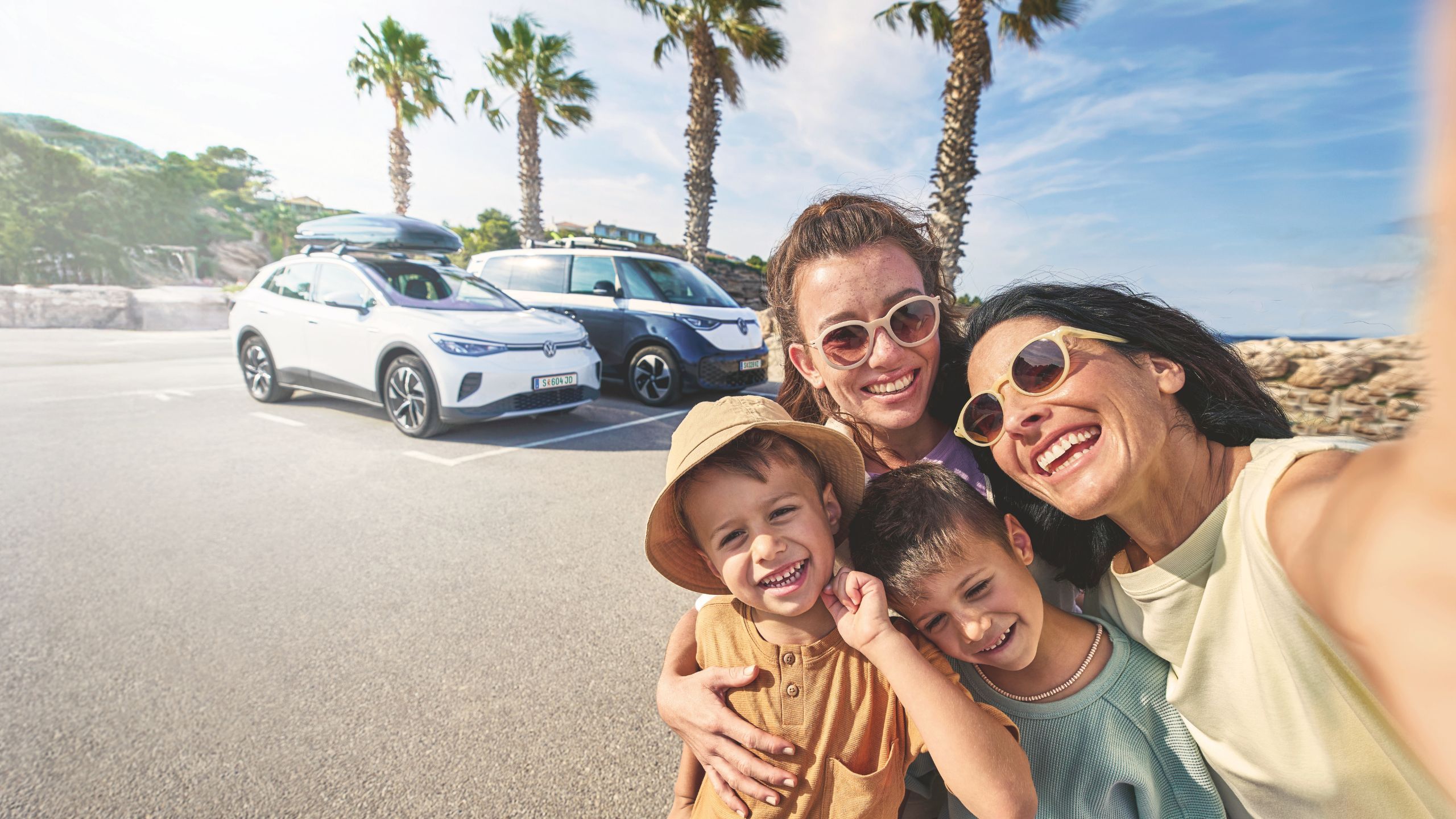 Eine Familie macht ein Selfie auf einem Parkplatz am Meer. Im Hintergrund stehen ein Volkswagen ID.3 und ein ID. Buzz nebeneinander.