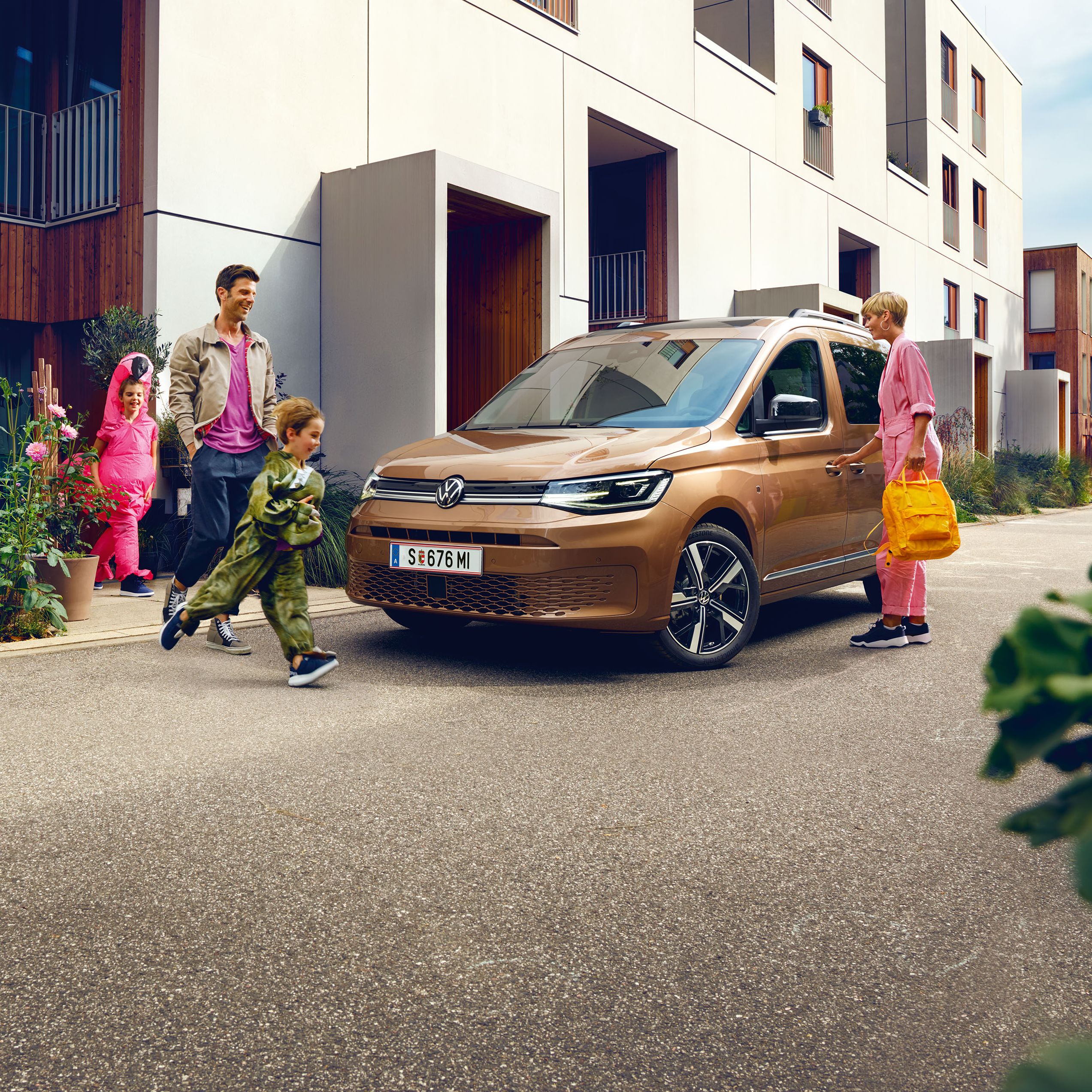 Eine junge Familie steigt vor der Wohnung in einen VW Caddy ein.