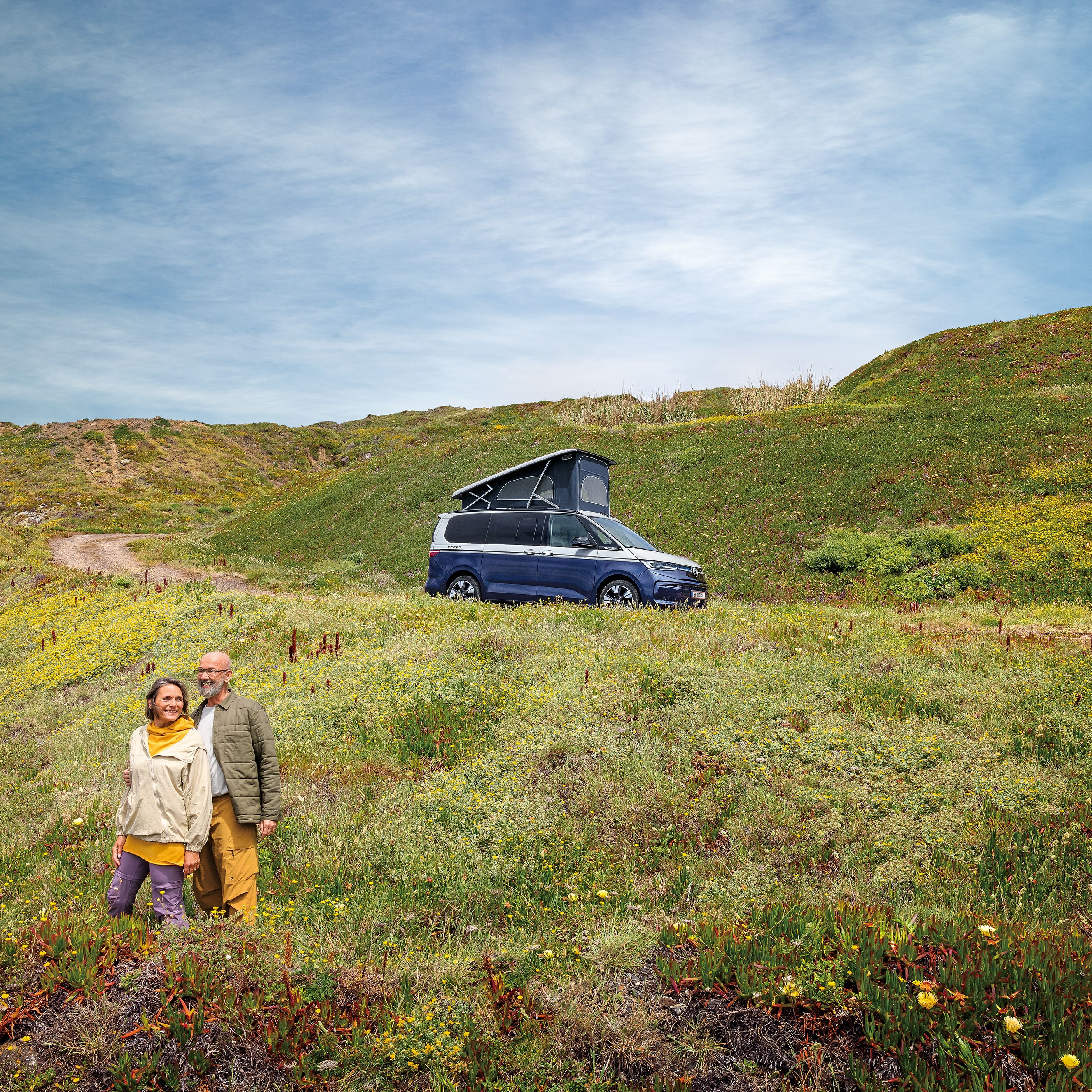 Ein VW California steht auf einer Schotterstraße am Meer