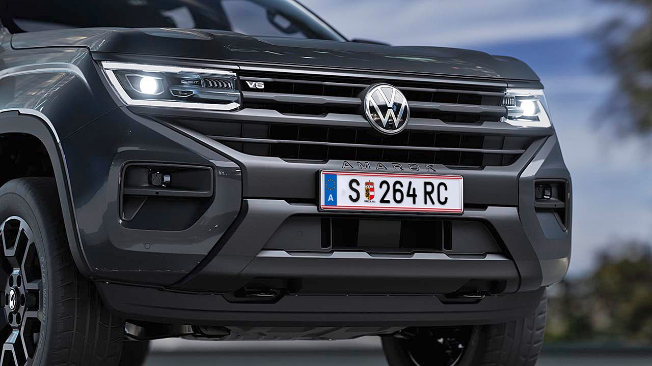 Nahaufnahme der Front eines grauen Volkswagen Amarok mit österreichischem Kennzeichen. Das Fahrzeug ist modern gestaltet und hat LED-Scheinwerfer. Das Kennzeichen zeigt die Buchstaben "SE" und die Zahlen "264 RC".